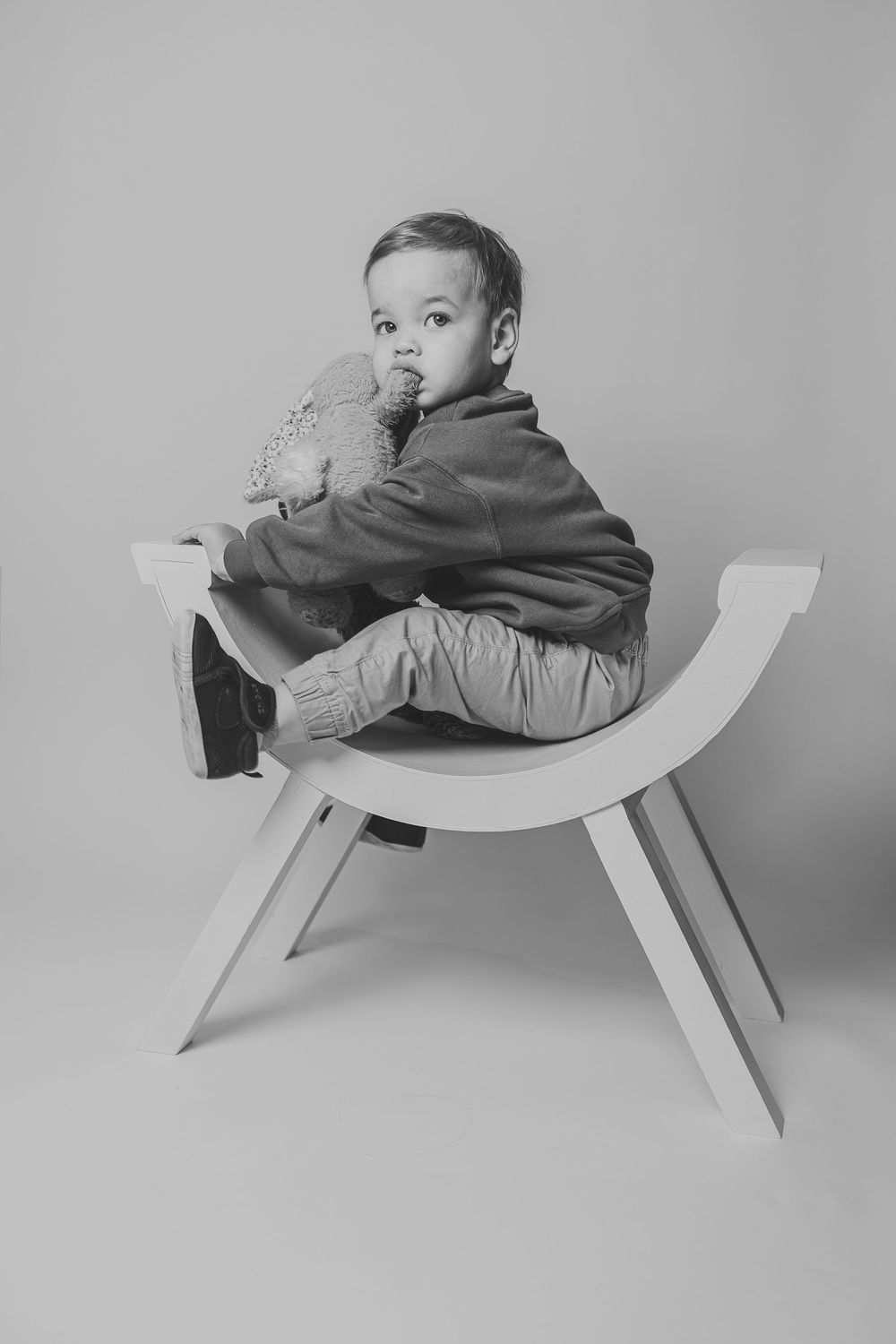 A minimalist curved wooden bench or chair shown in a series of black and white photographs against a plain background.