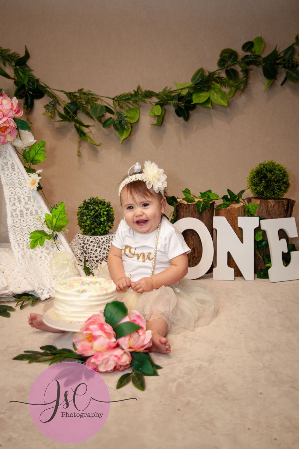 First birthday setup with floral decorations, cake, and 'ONE' letters display.