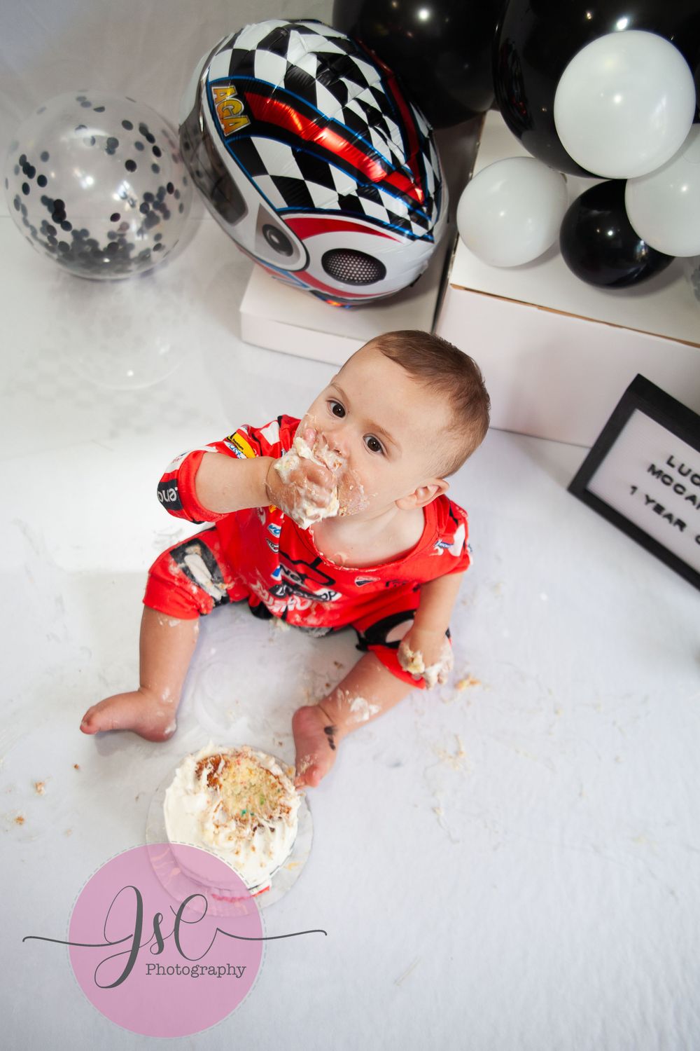 Baby in red racing outfit enjoying a cake smash photo session with black and white checkered decorations.