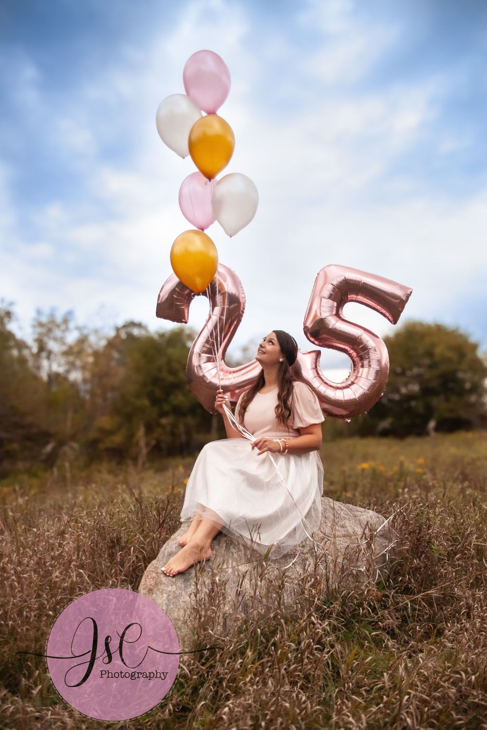 Birthday celebration in field with rose gold number balloons and cloudy sky background.