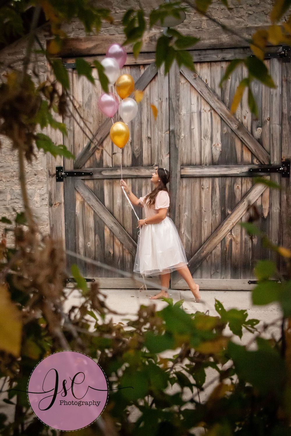 White dress celebration photoshoot with balloons against rustic wooden barn door.
