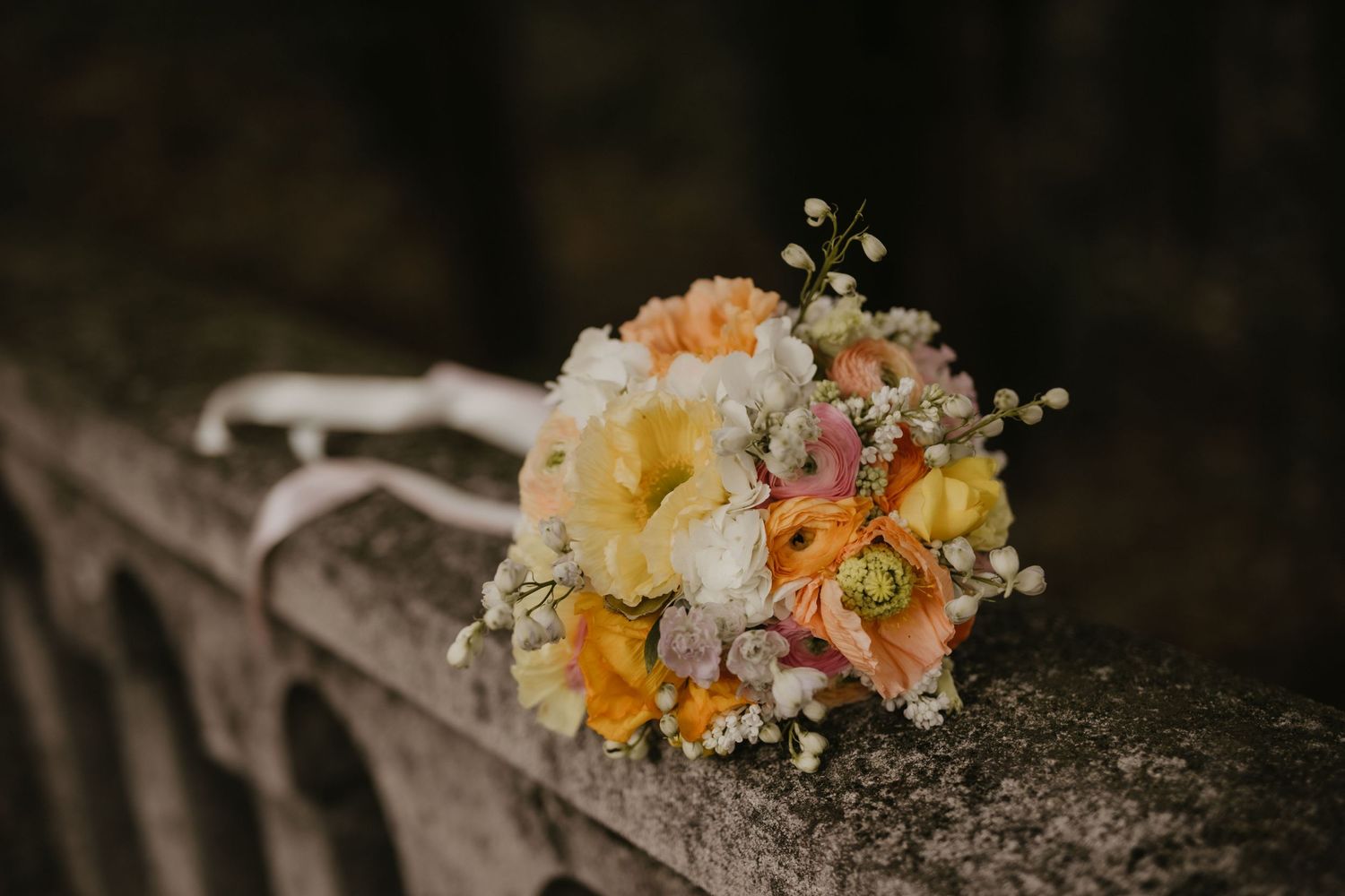 Delicate bouquet with peach and yellow flowers resting on stone railing.
