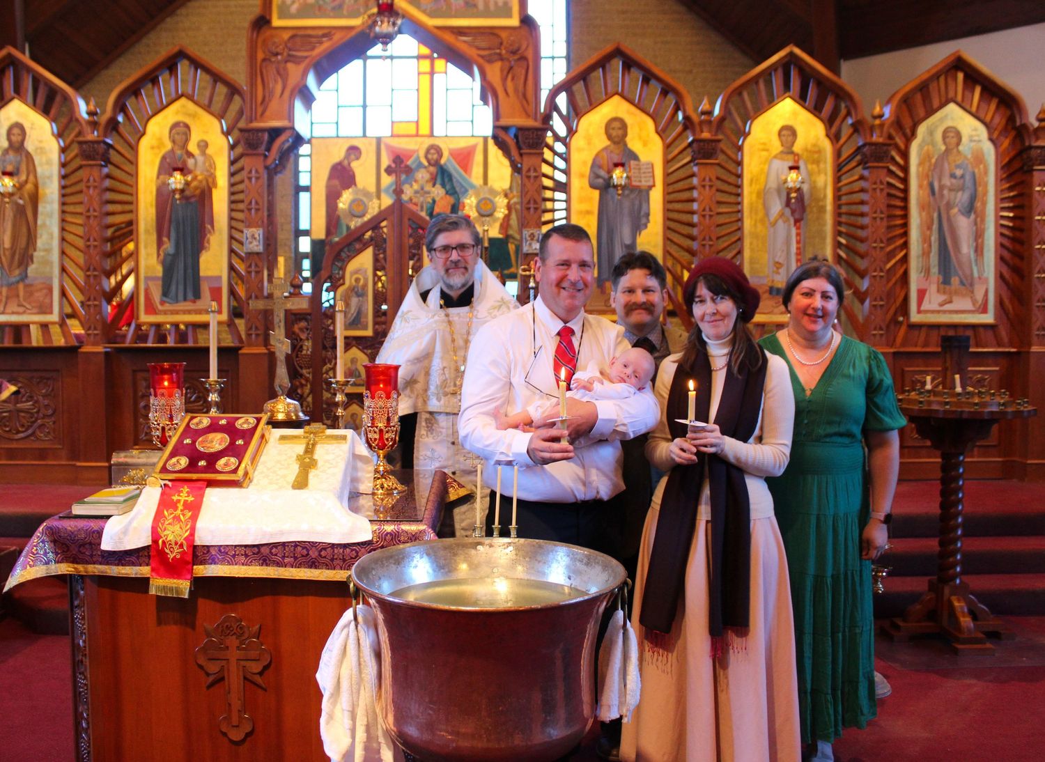 A baptism ceremony in an Orthodox church with religious icons and candles.