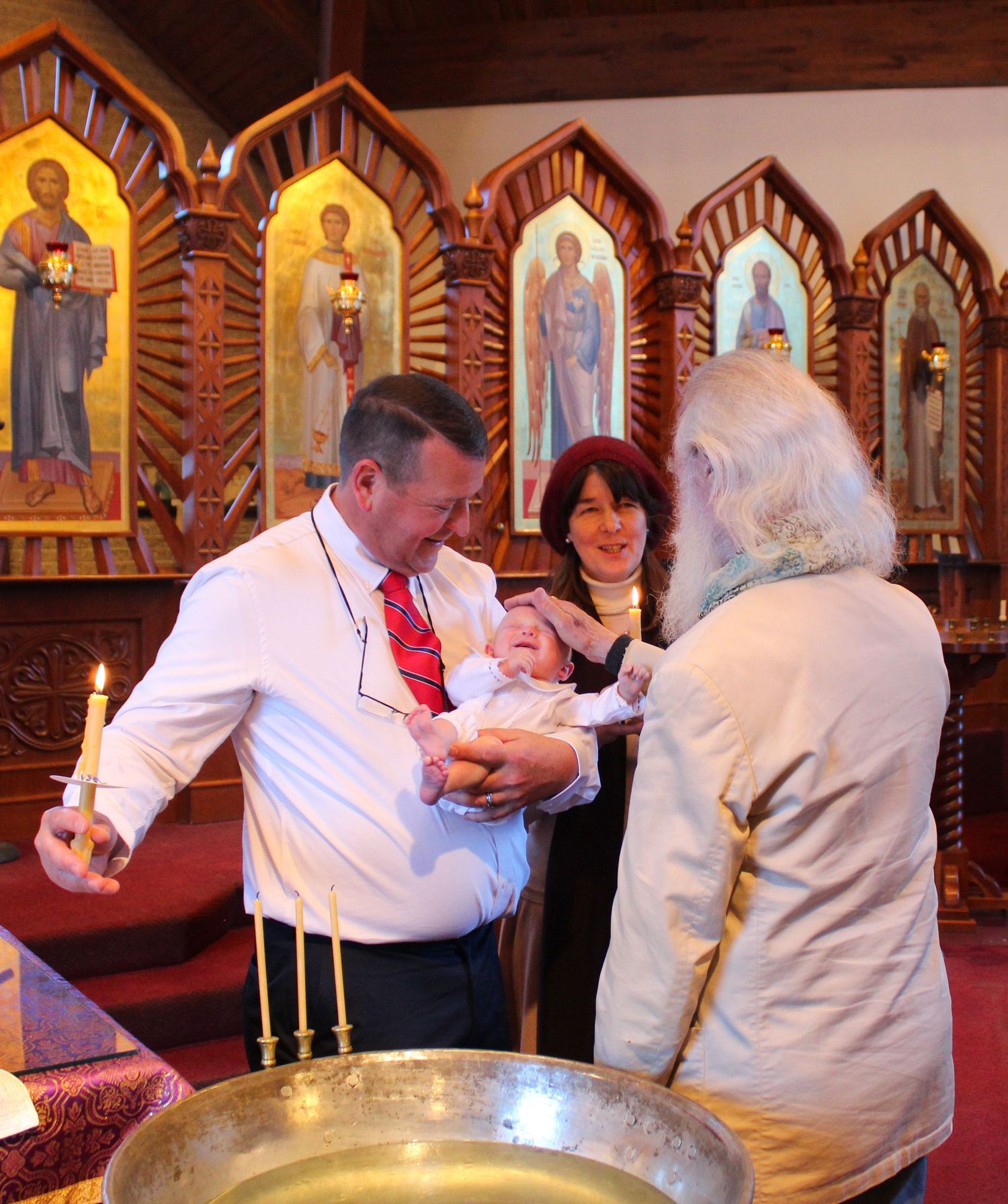 A baptismal ceremony taking place in front of ornate religious icons in a church.
