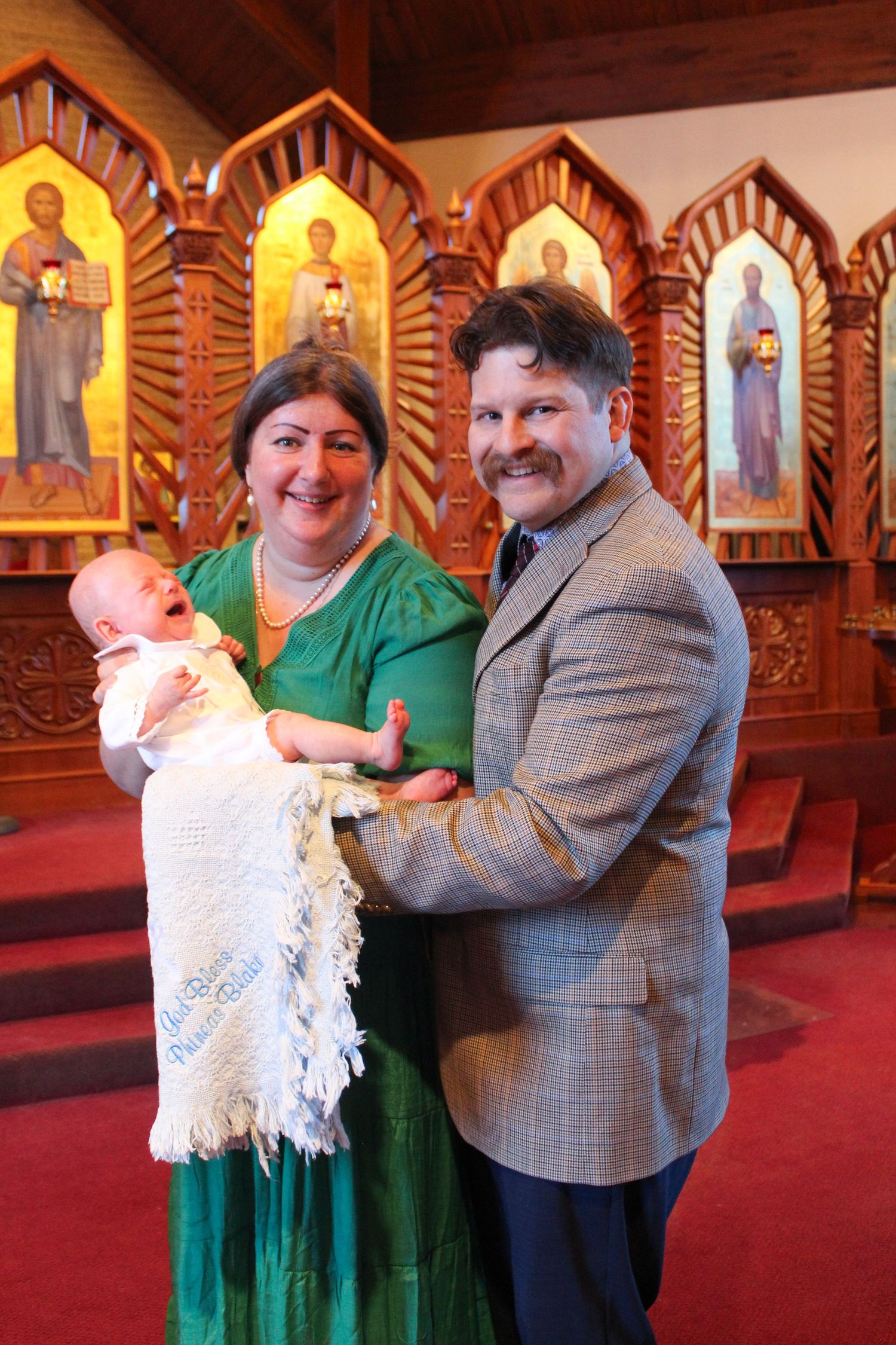 Family celebrating a baptism ceremony in front of ornate church icons.