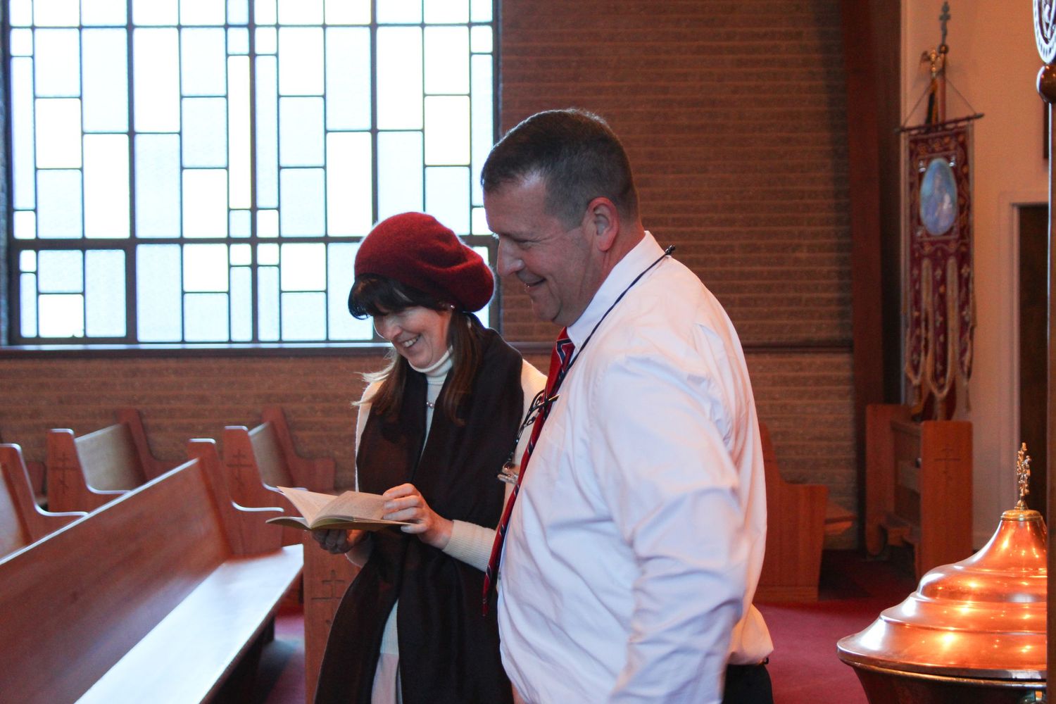 People standing in church pews reviewing service materials during ceremony.