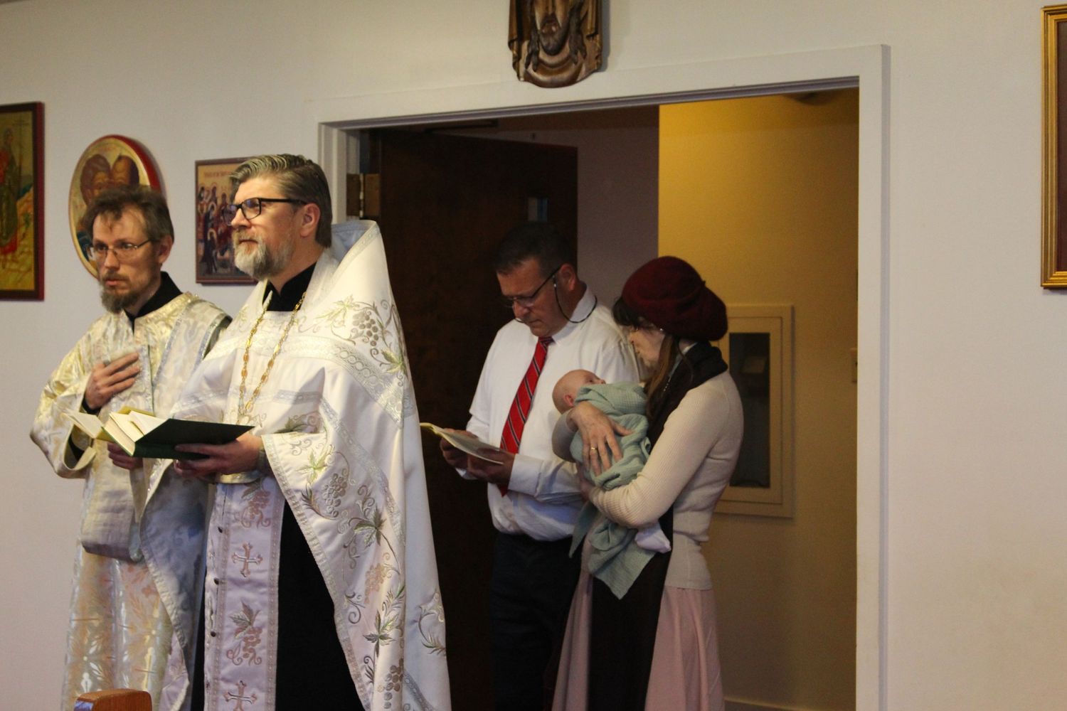 Religious ceremony participants in white robes and formal attire standing near church doorway.