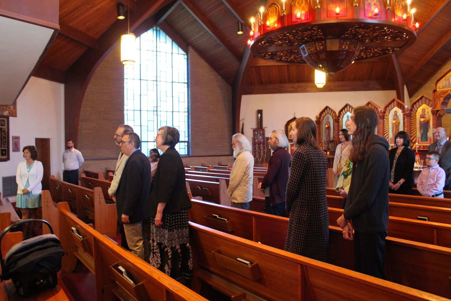 Church interior with people standing in wooden pews under dramatic lighting.