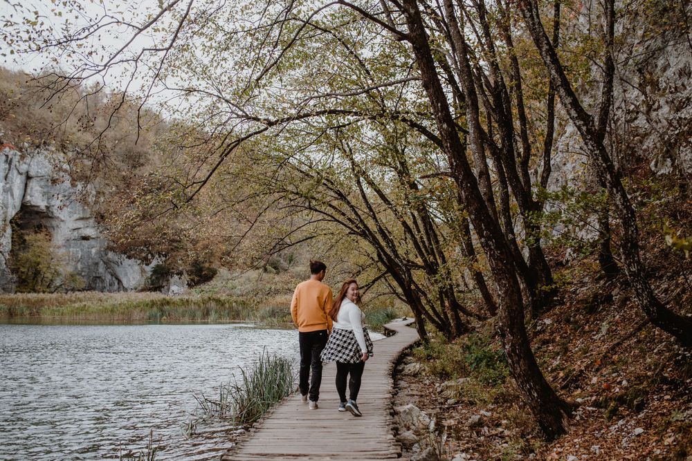 Wide shot of the couple exploring Plitvice National Park during autumn, surrounded by vibrant fall scenery.