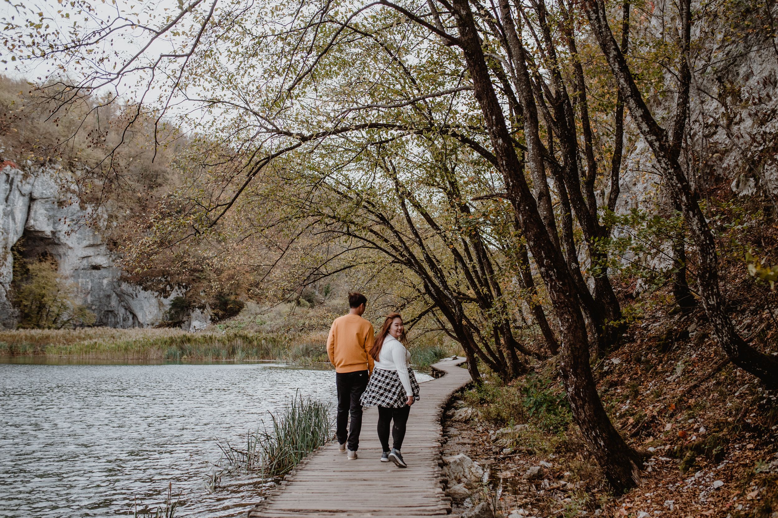 Wide shot of the couple exploring Plitvice National Park during autumn, surrounded by vibrant fall scenery.