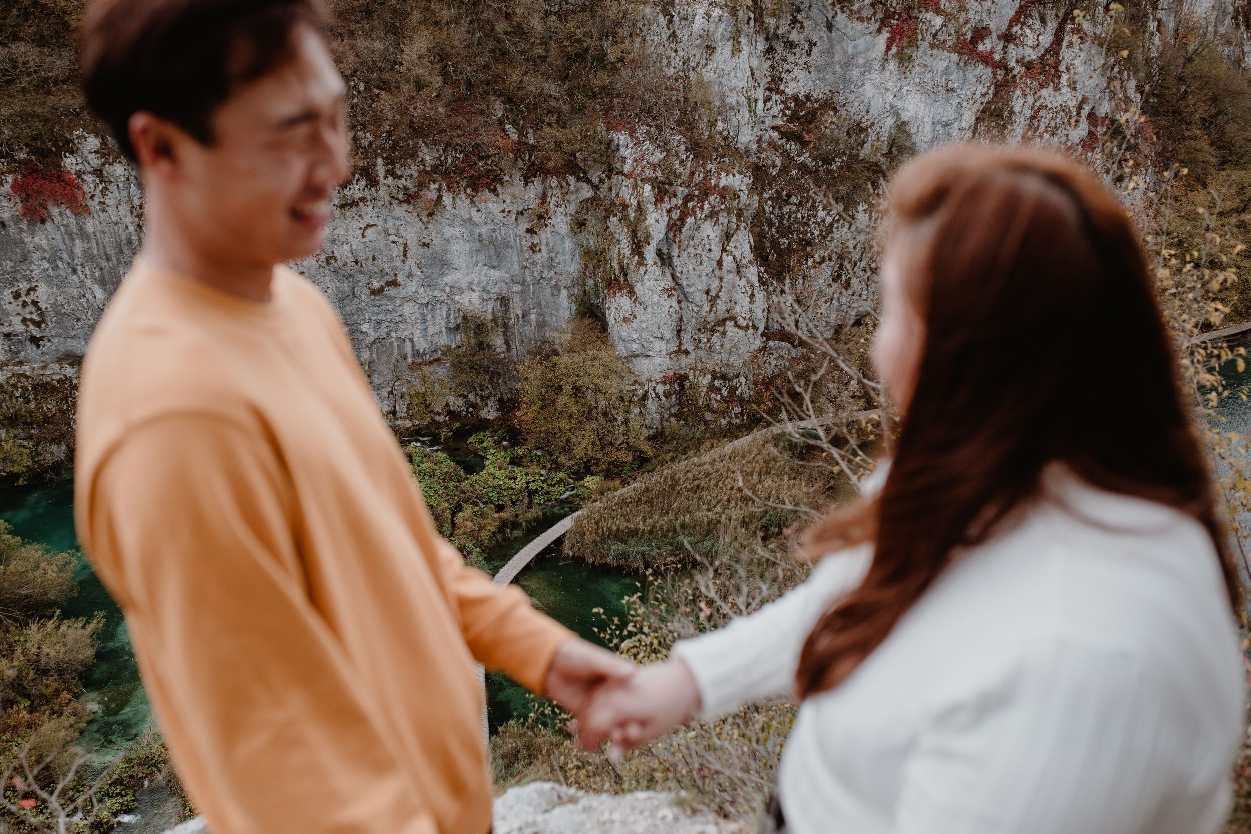 Couple in the foreground, out of focus, with the scenic wooden paths of Plitvice National Park in the background.