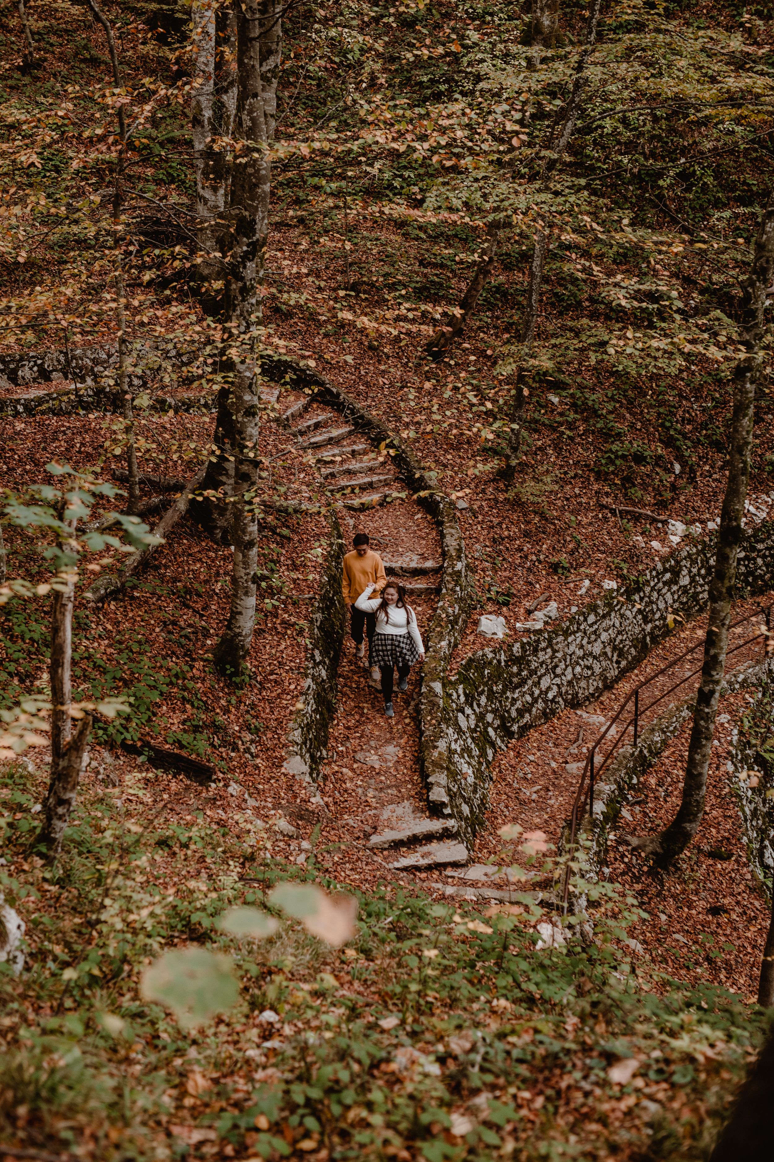 Couple walking together on forest stairs, captured from the front, with fall scenery of Plitvice National Park.