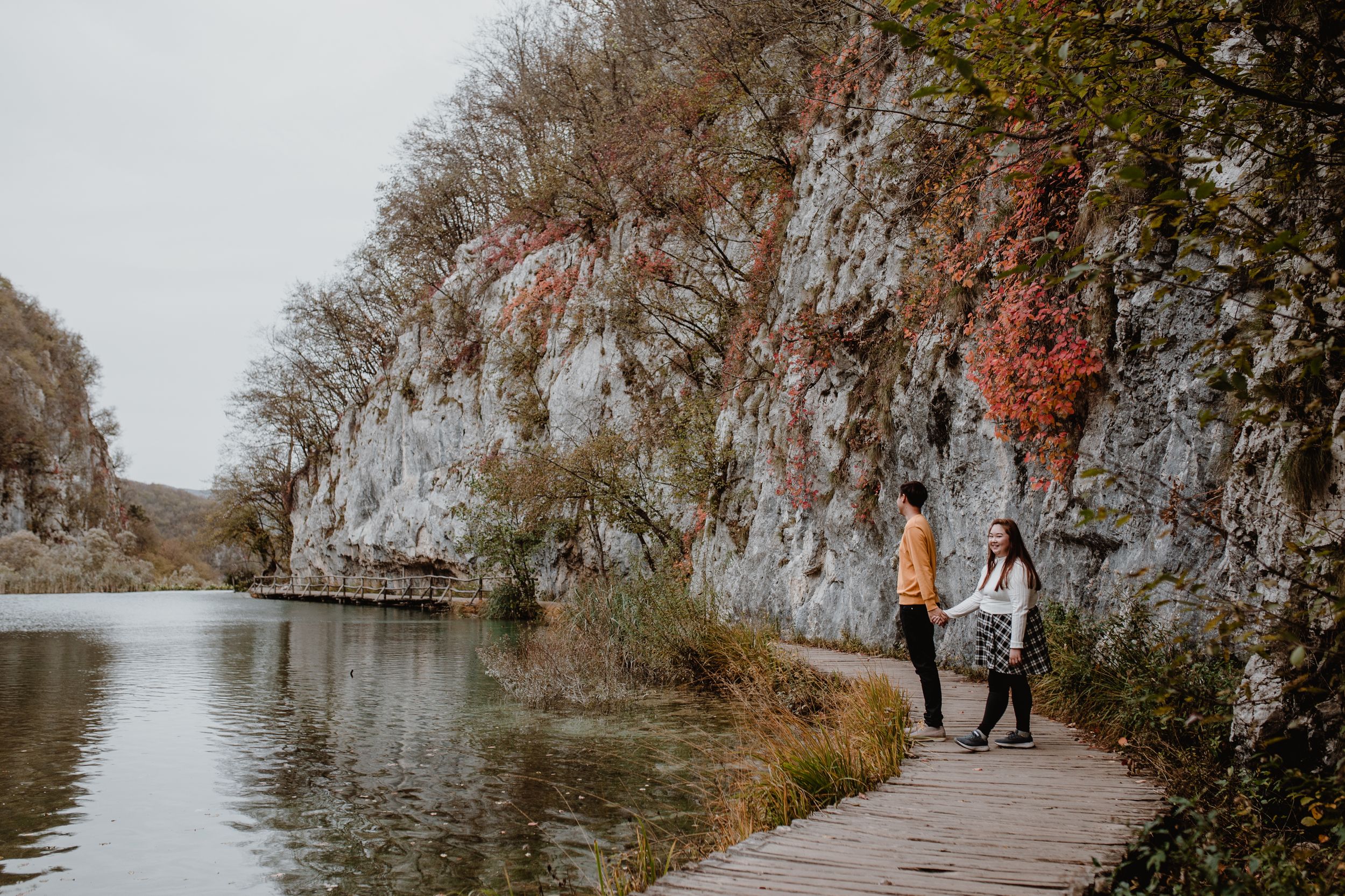 Wide shot of a couple exploring the scenic trails of Plitvice National Park, surrounded by the natural beauty.