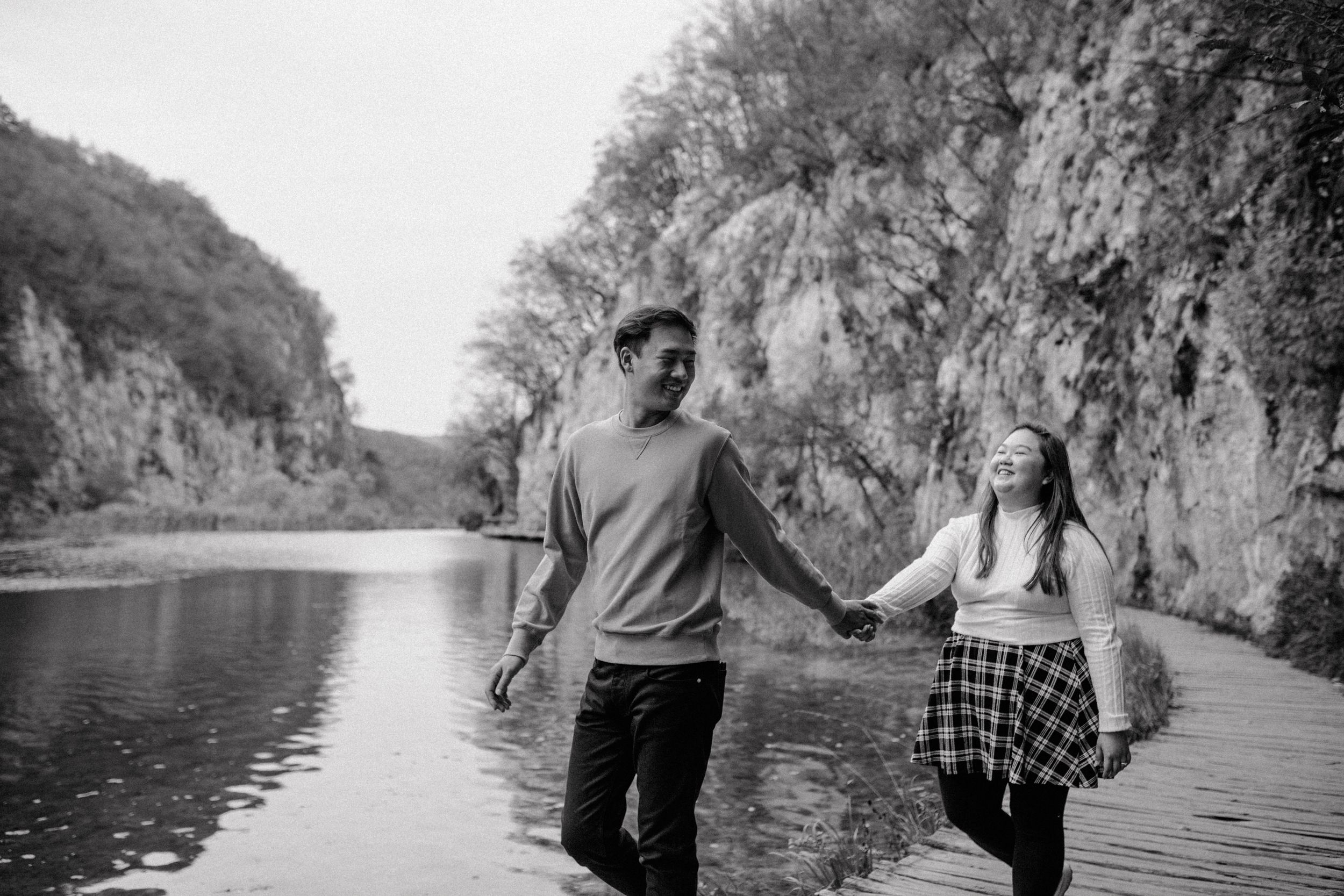 Black and white photo of a couple laughing and holding hands while walking through Plitvice National Park.