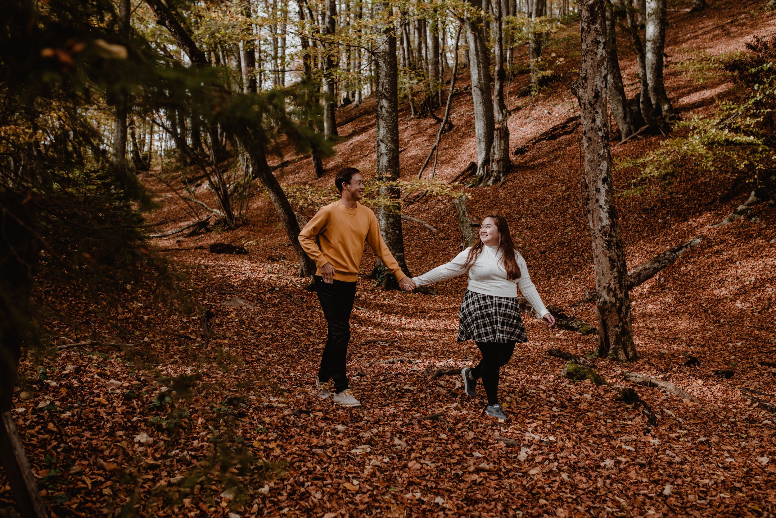 photo of thCouple holding hands walking through the vibrant autumn forest at Plitvice National Park in Croatia.
