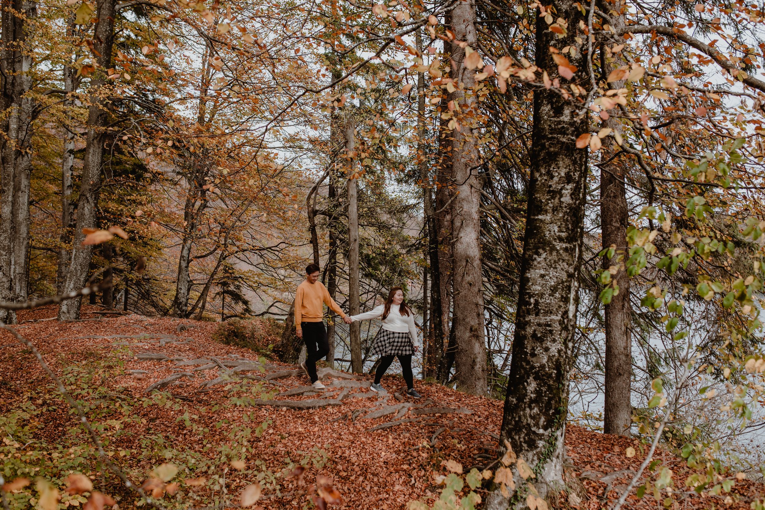 Couple strolling hand in hand through the vibrant autumn forest at Plitvice during their vacation photoshoot.