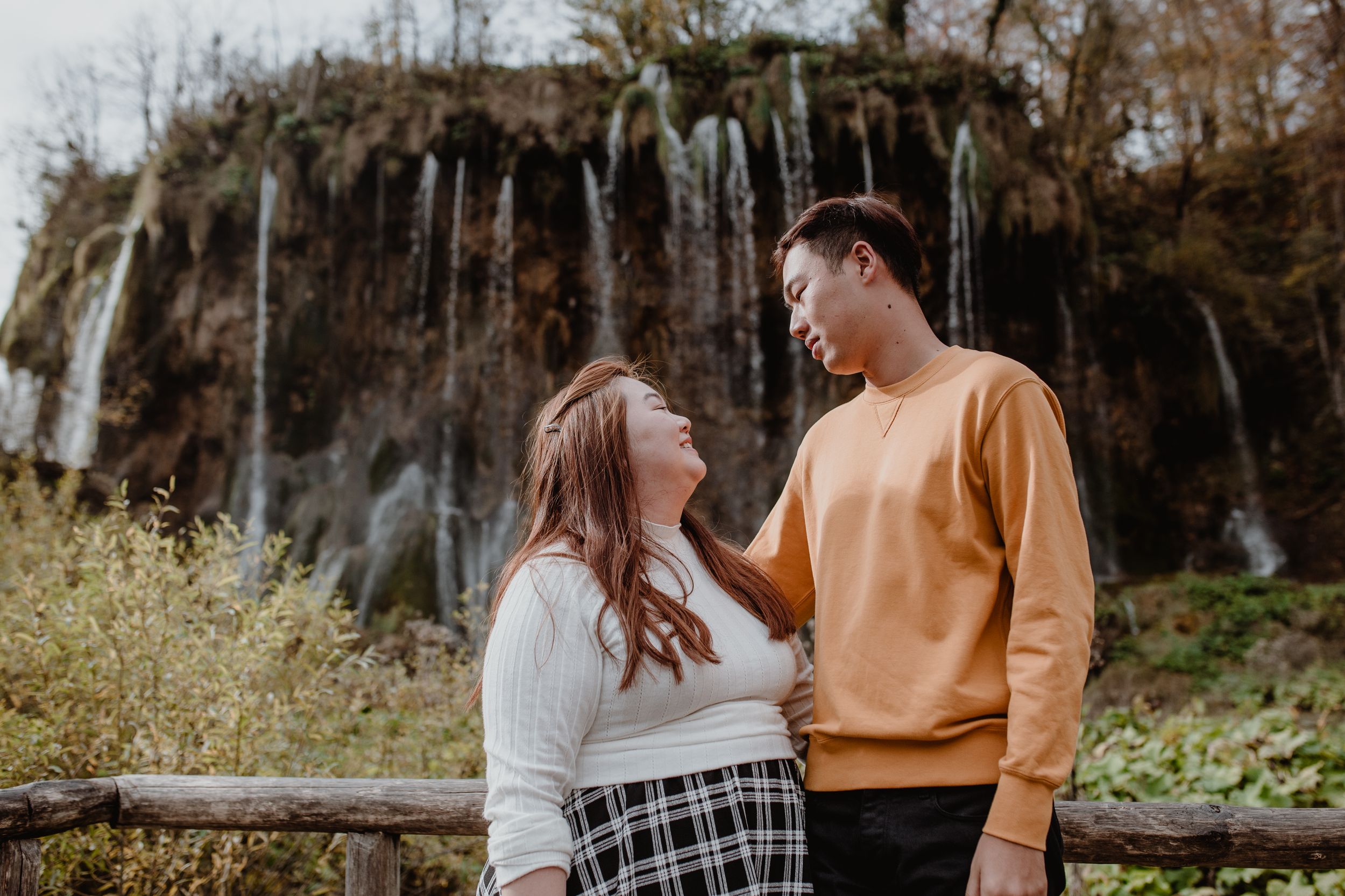 Couple gazing at each other with a majestic waterfall in the background during their vacation photoshoot at Plitvice.