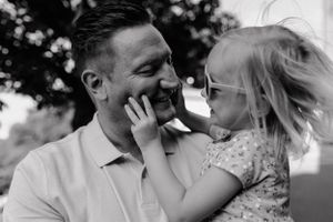 Close-up of a child playfully touching their dad's face while being held, capturing a joyful family moment.
