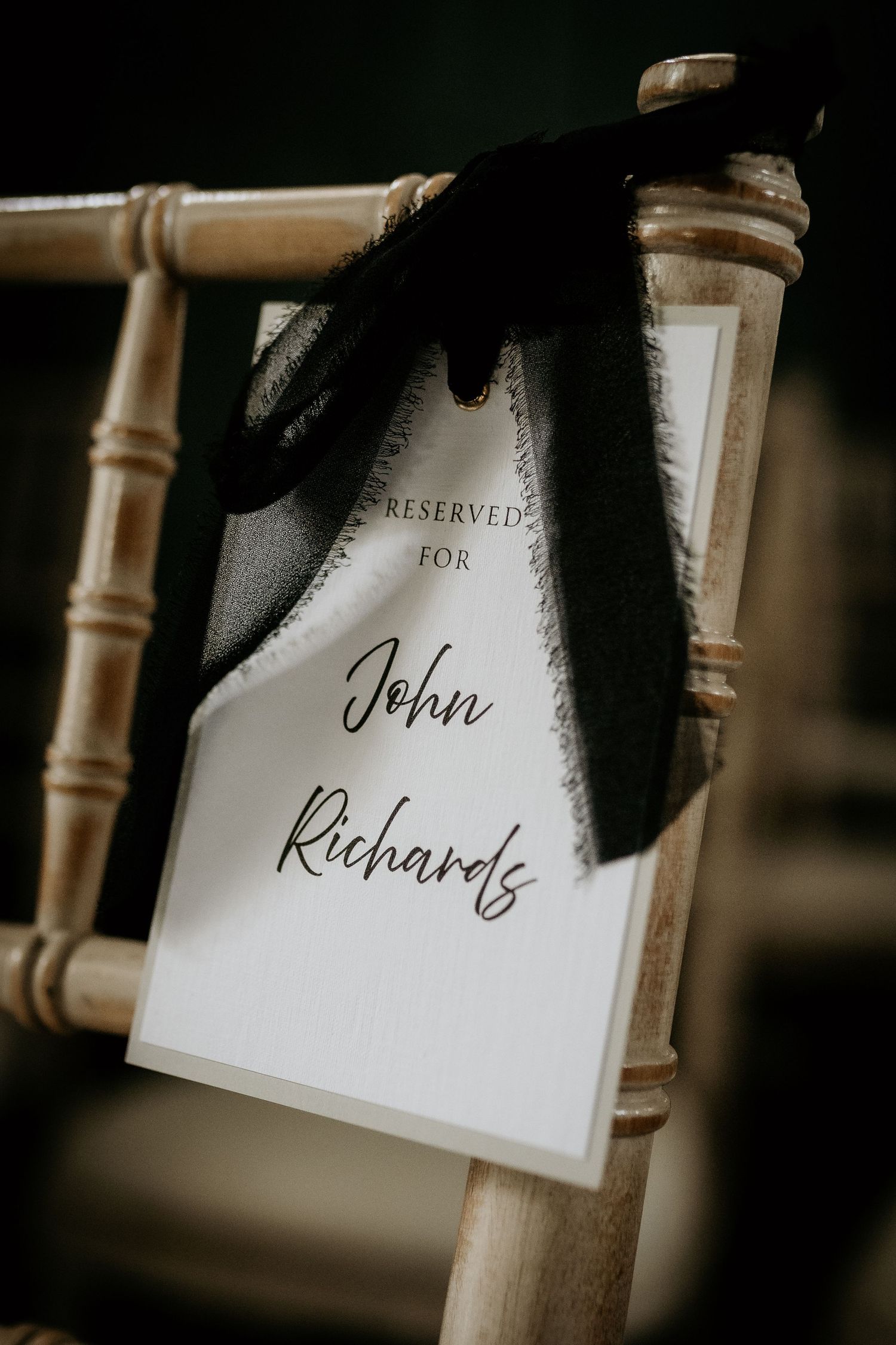 A series of name cards or place cards with elegant calligraphy hang from wooden chairs at an event setup.