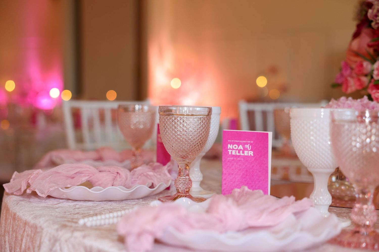 Elegant pink wedding reception table setting with crystal goblets, pearls, and floral centerpieces.