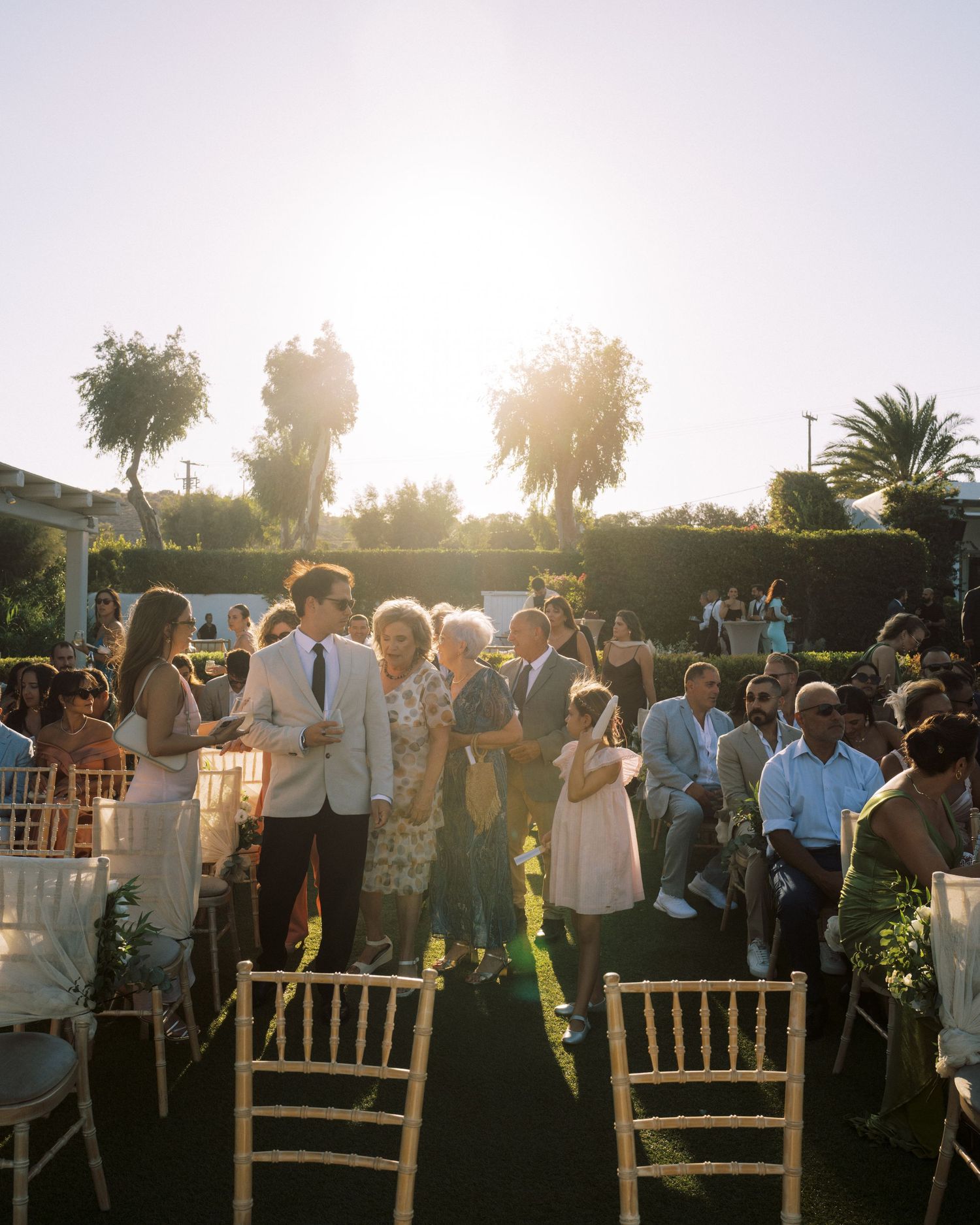 Black and white photograph of wedding guests gathered on a grassy hillside under tall trees.