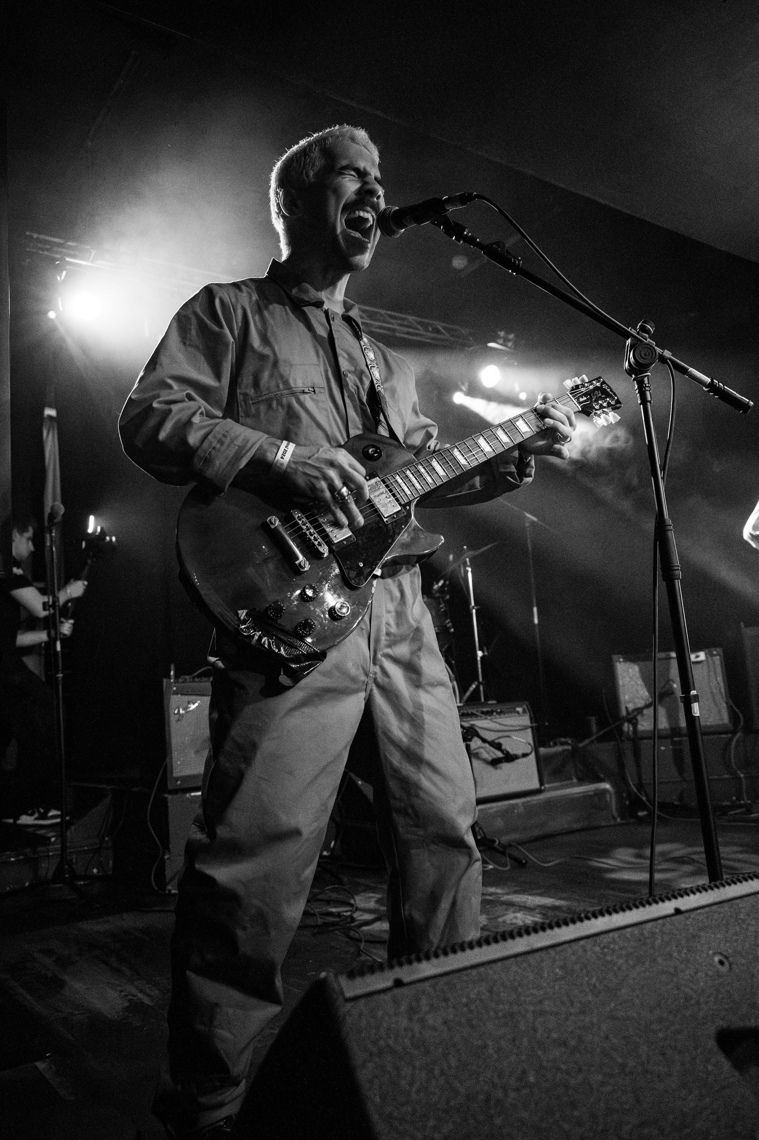 Guitarist performs energetically on stage with bright spotlights in black and white photography.