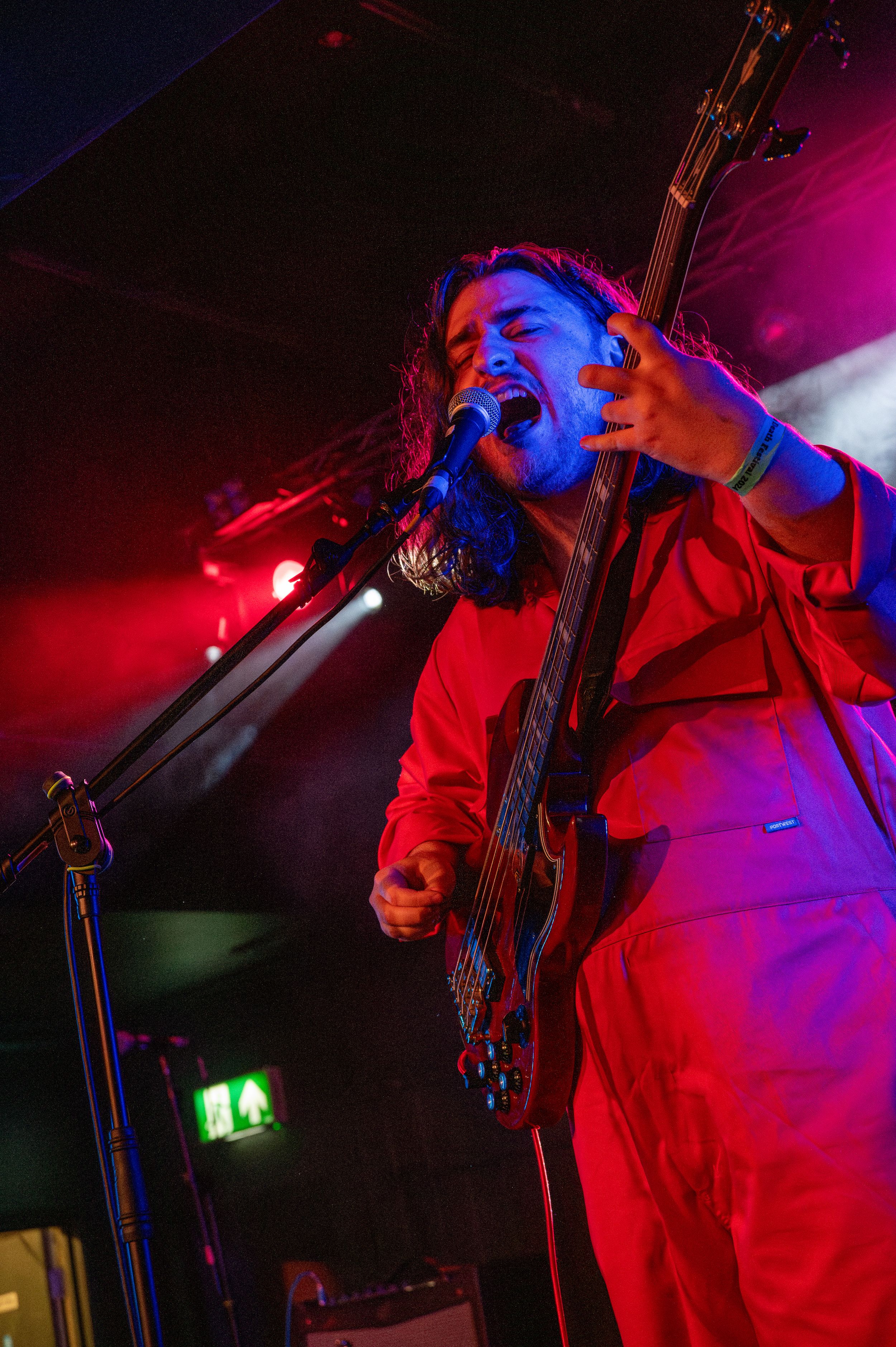 Bass player in red outfit performs under dramatic red stage lighting.