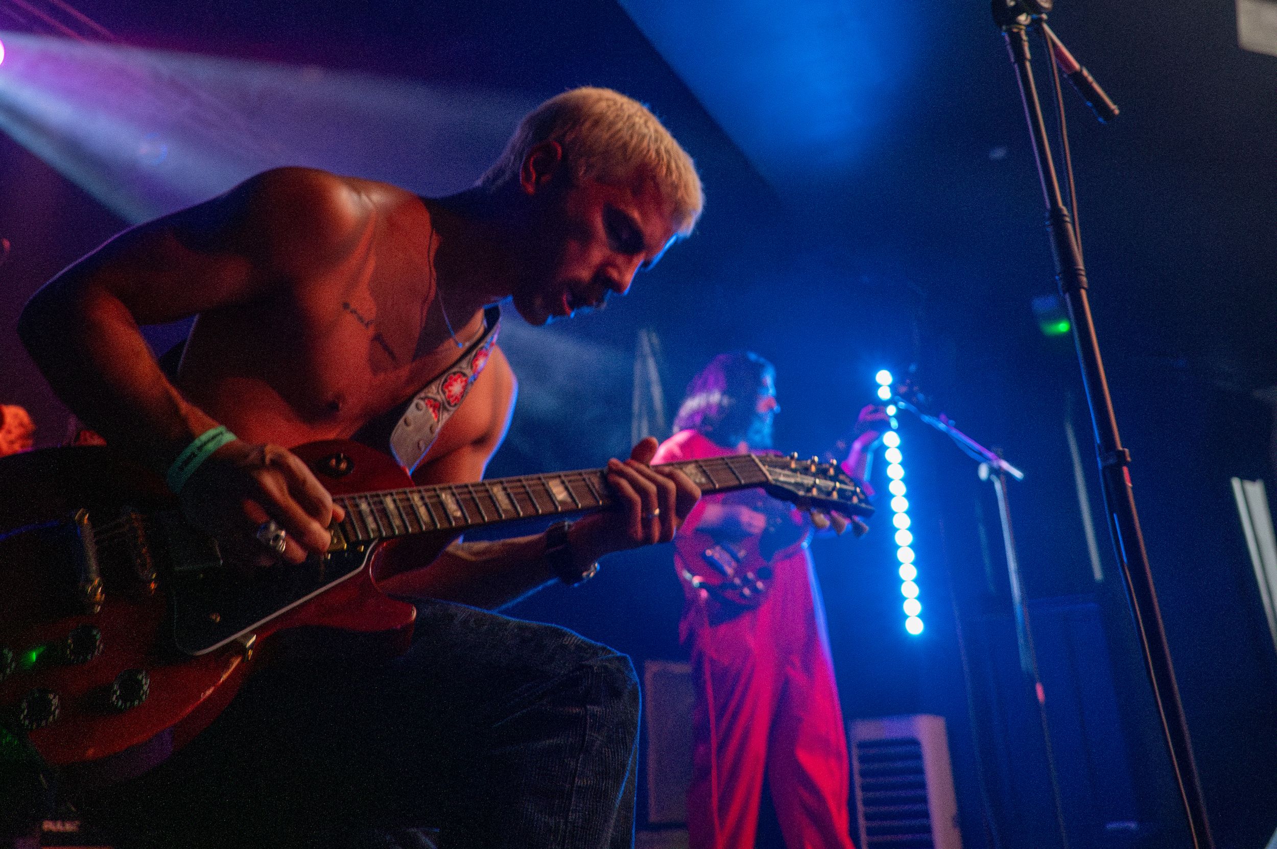 Guitar player bathed in dramatic blue and red stage lighting during energetic performance.