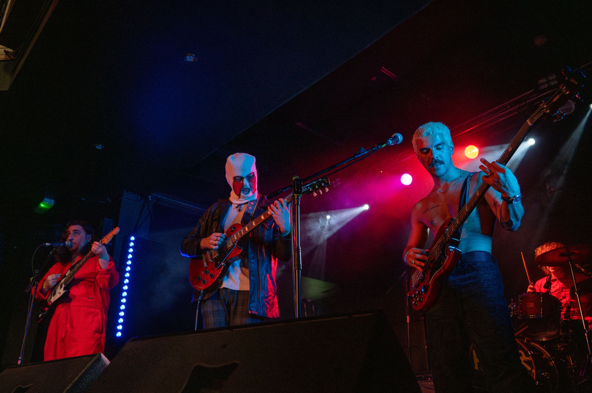 Band members performing on stage with blue and red lighting effects.