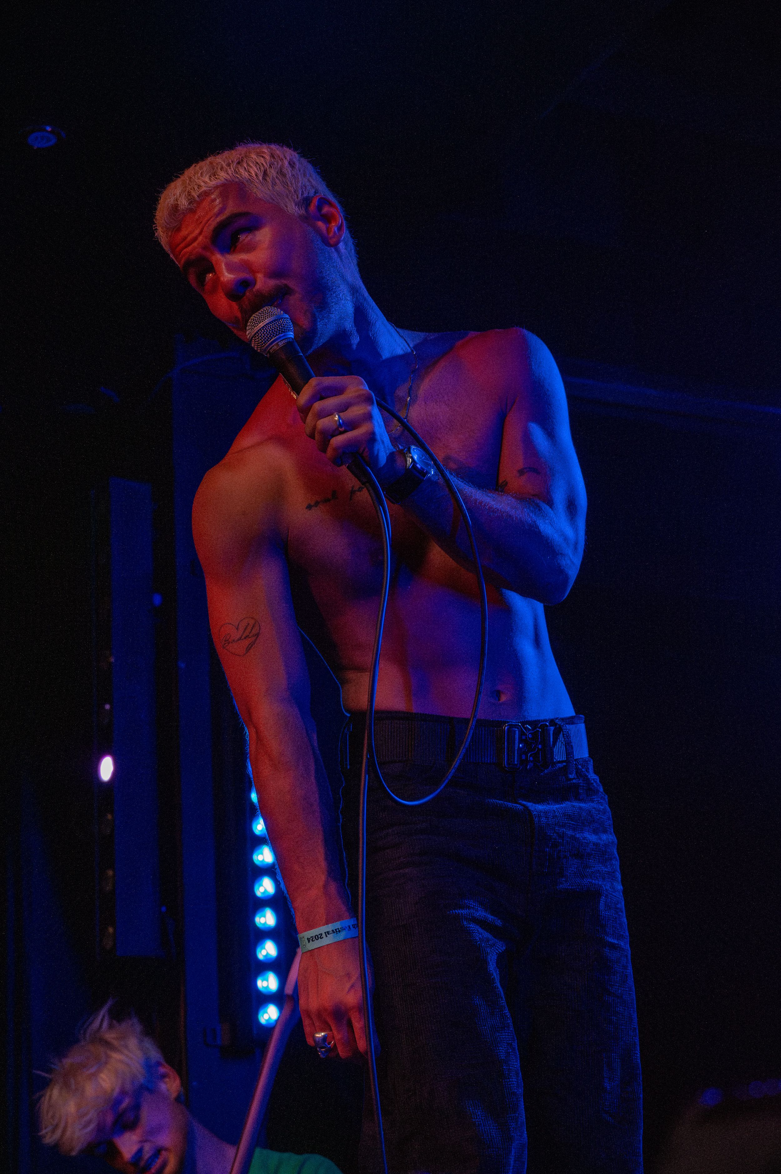 Performer singing into microphone under dramatic colored stage lighting.