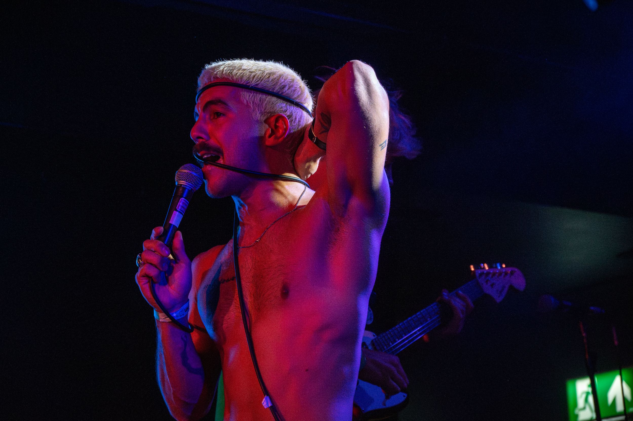 Concert performer singing on stage illuminated by red and blue lights.