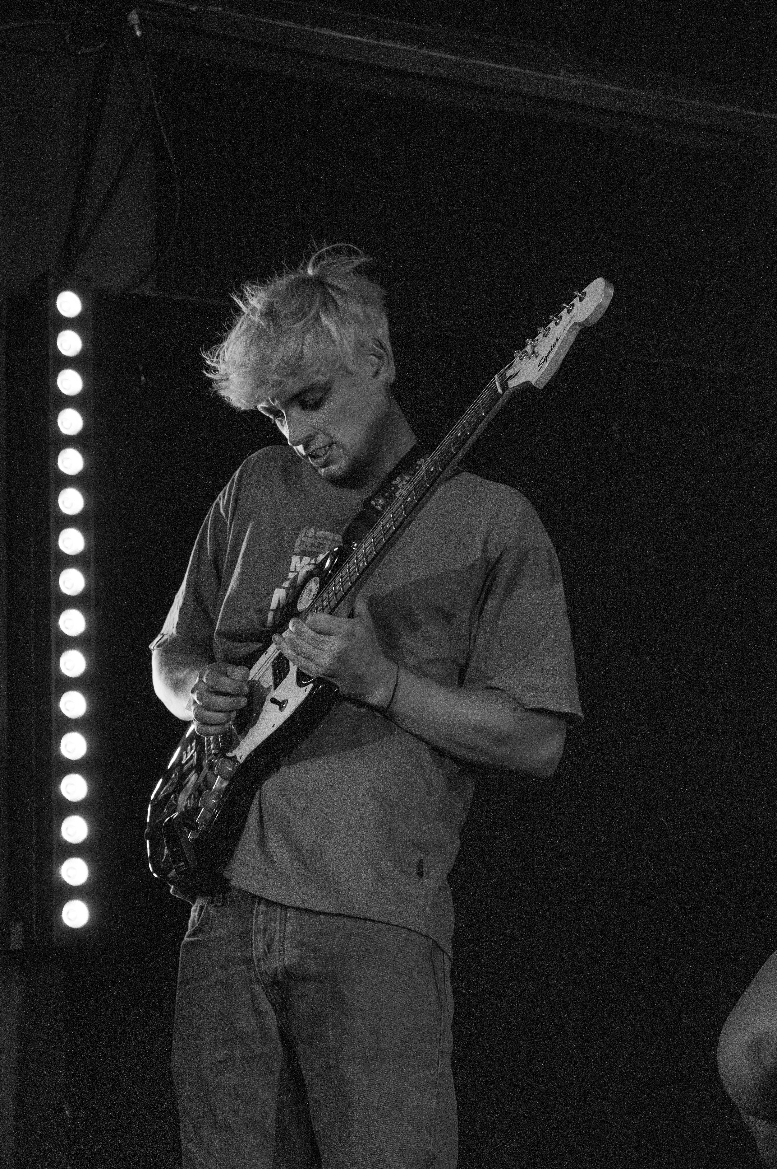 Black and white photo of musician playing electric guitar under stage lights.