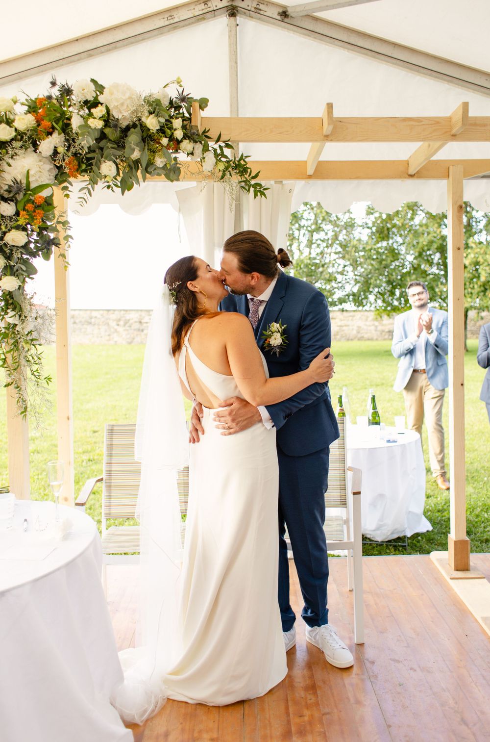 Romantic moment between newlyweds under floral arch at outdoor tent wedding.
