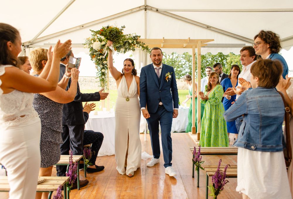 Wedding guests applauding couple during ceremony processional in white tent venue.