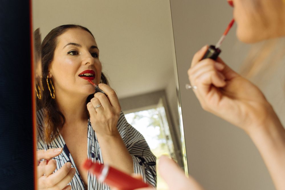 Person applying red lipstick in mirror reflection.