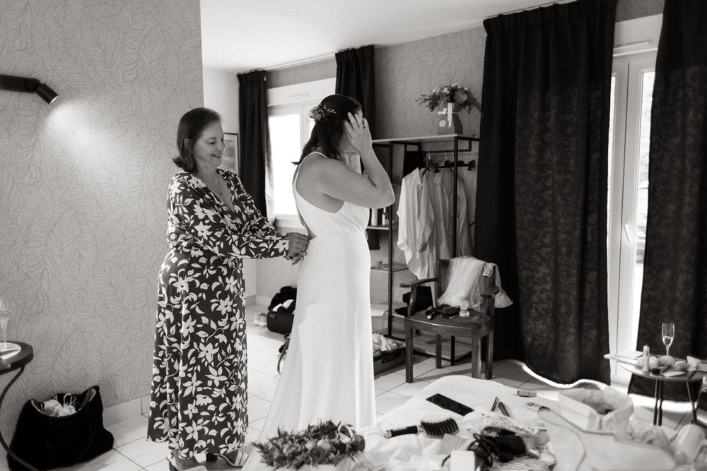 Wedding preparation scene in black and white showing dress fitting in bedroom.