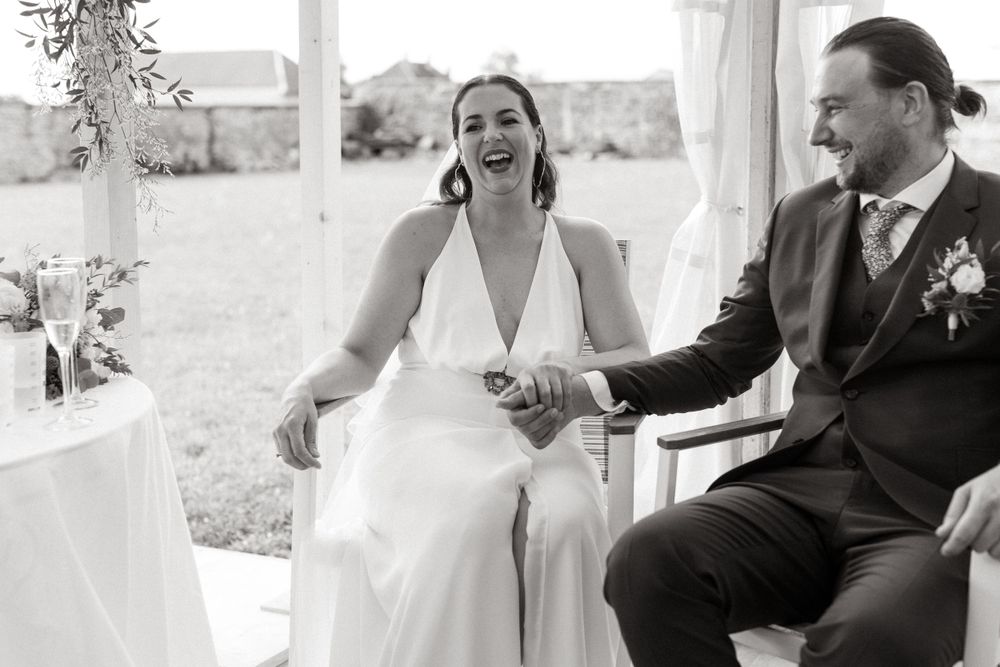 A couple shares a joyful moment while seated during their outdoor wedding ceremony.