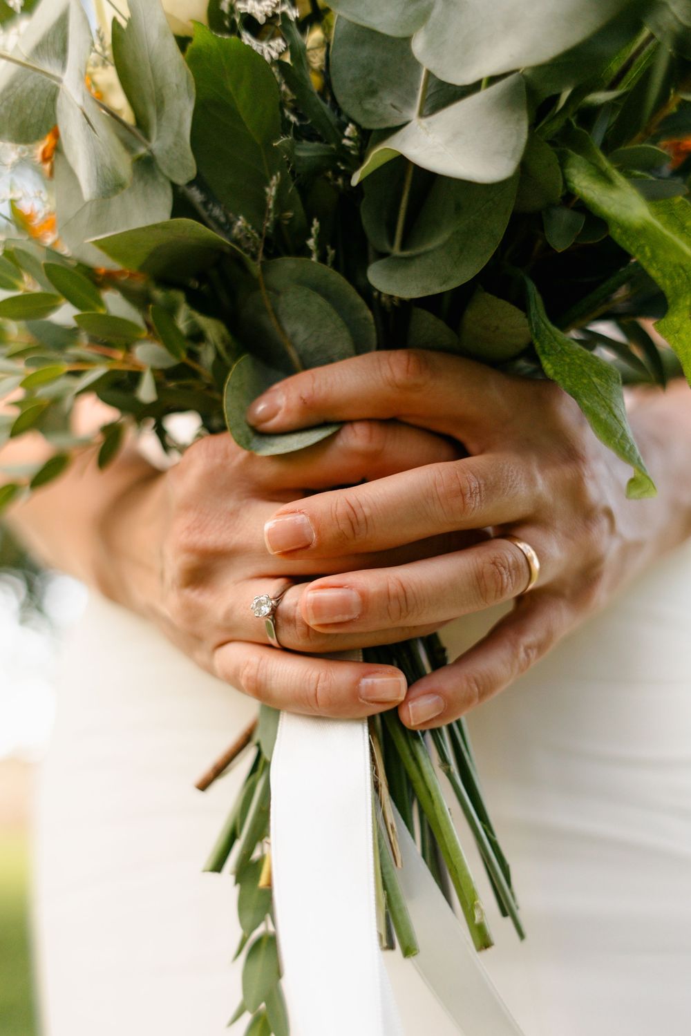 Close up of hands holding a white and green floral wedding bouquet with eucalyptus leaves.