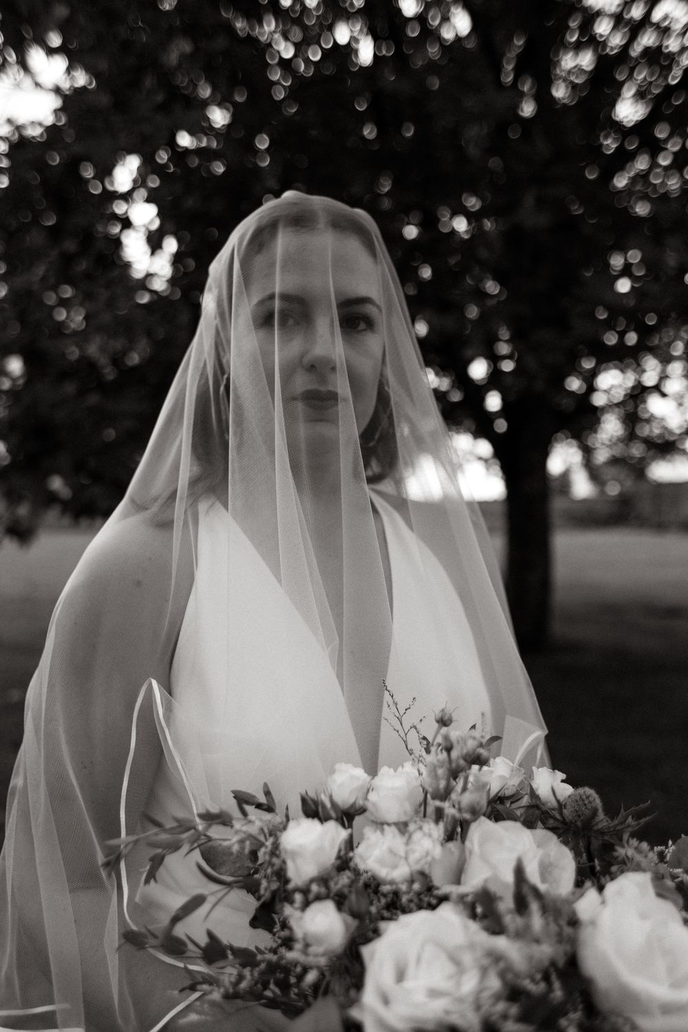 An elegant bride in a white dress holds a romantic bouquet of roses under a flowing veil.