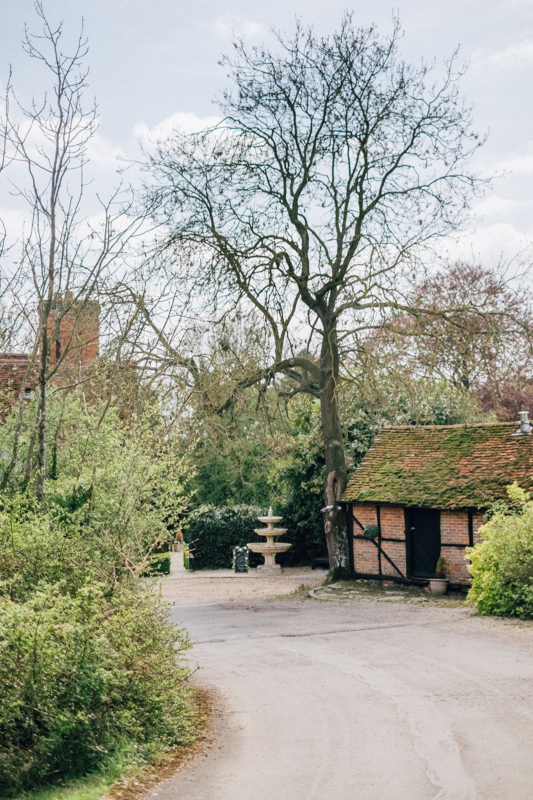 Winding garden path with bare trees and traditional brick buildings in rural setting.