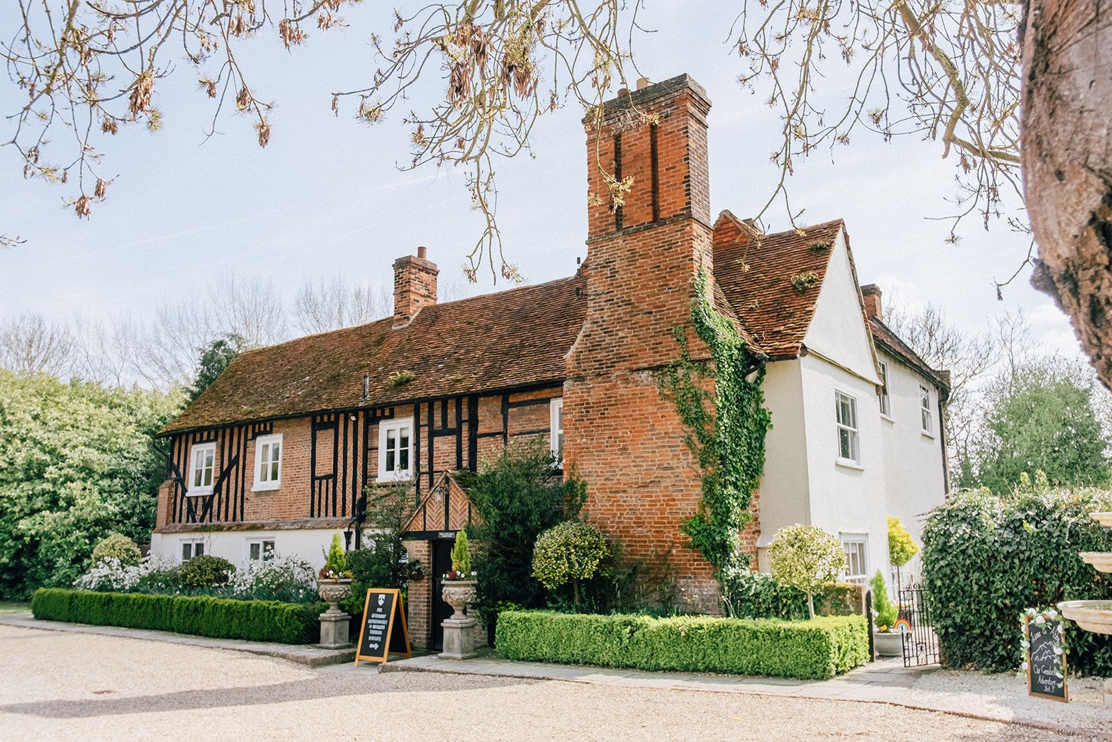 Traditional English Tudor-style building with red brick chimneys and white-painted walls nestled among hedges.
