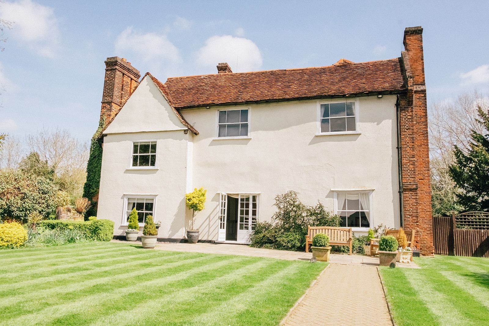 White country house with red brick chimneys and manicured lawn featuring a straight garden path.