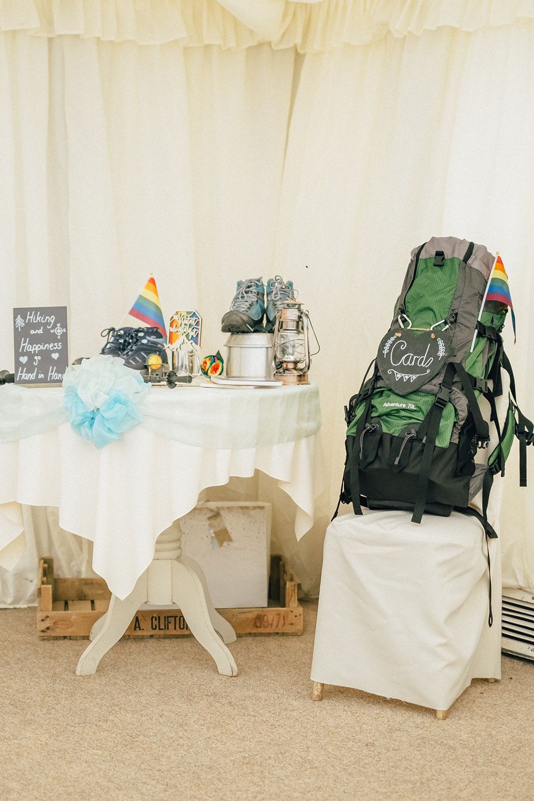 Wedding welcome table with hiking backpack and adventure-themed decorations in a white tent setting.