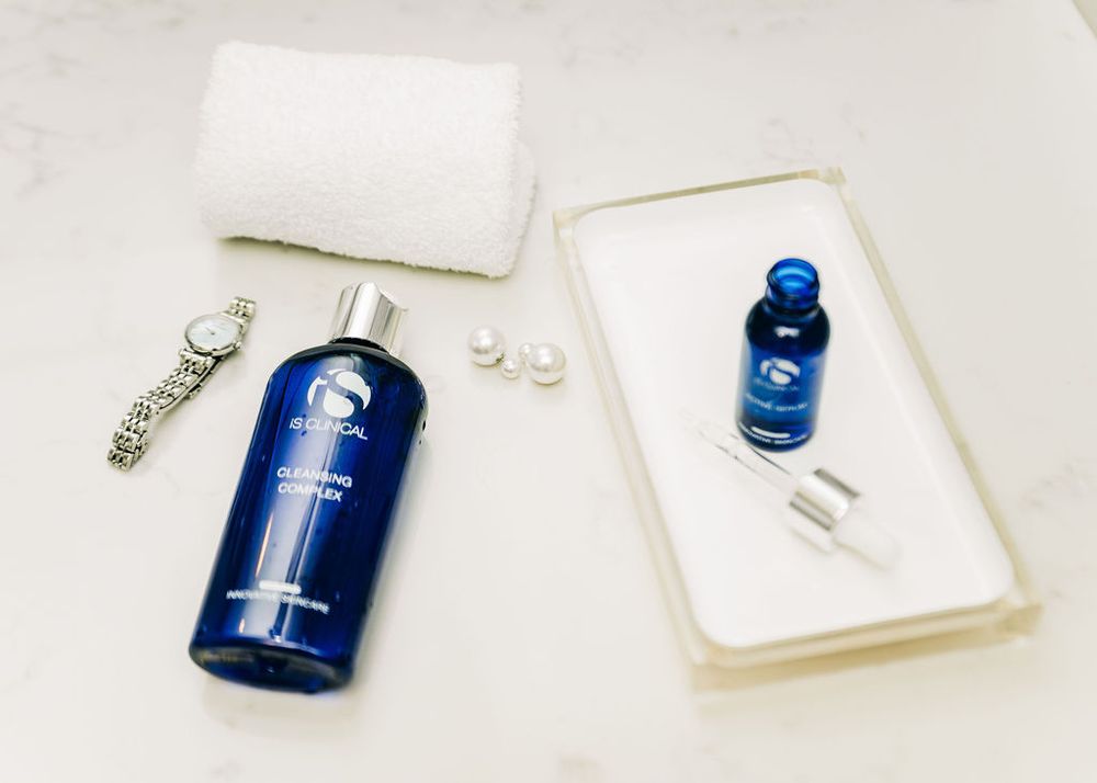 Minimalist flatlay of blue skincare bottles and pearls on white ceramic tray.