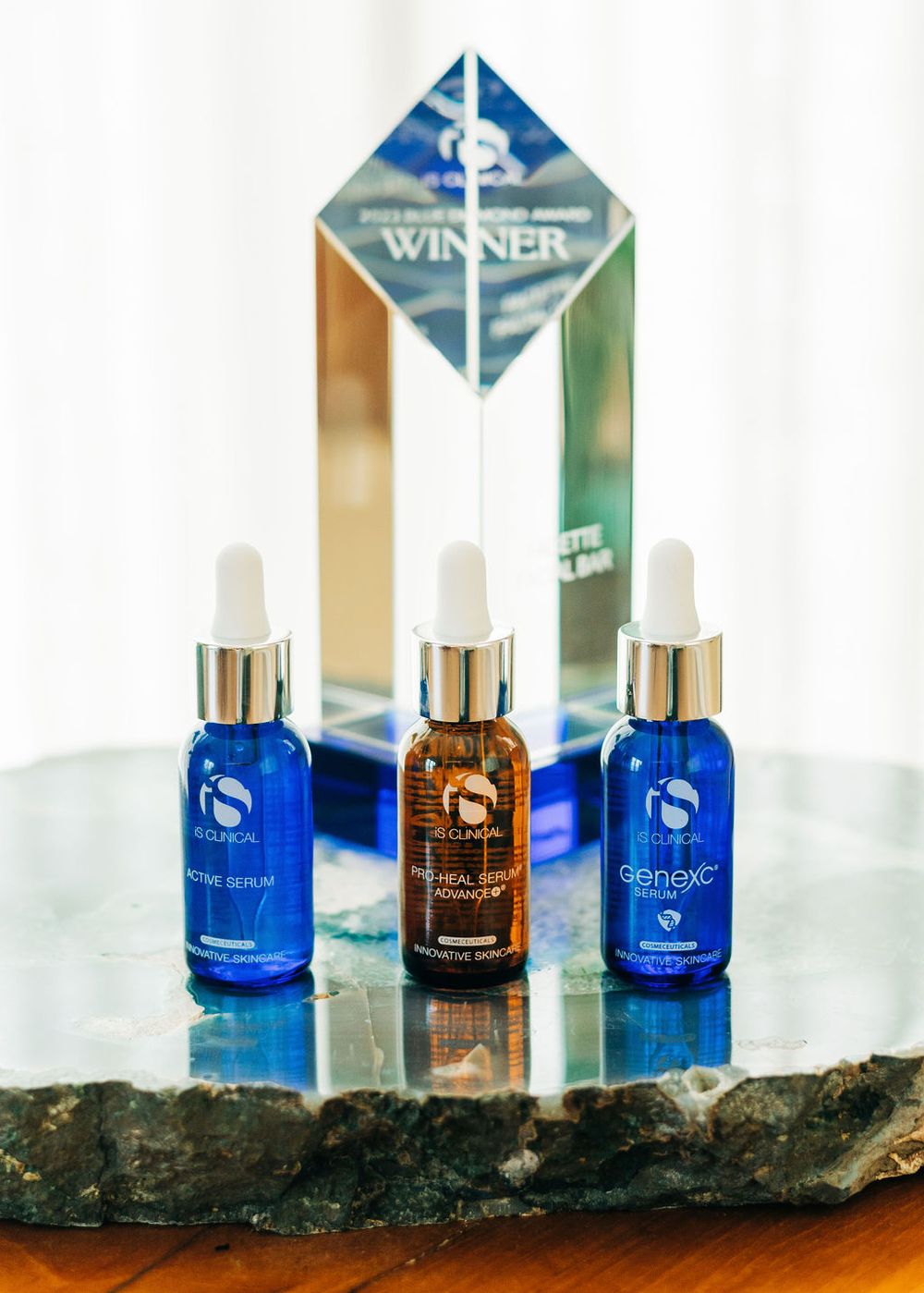 Elegant crystal award trophy displayed with three serum bottles in blue and amber glass.