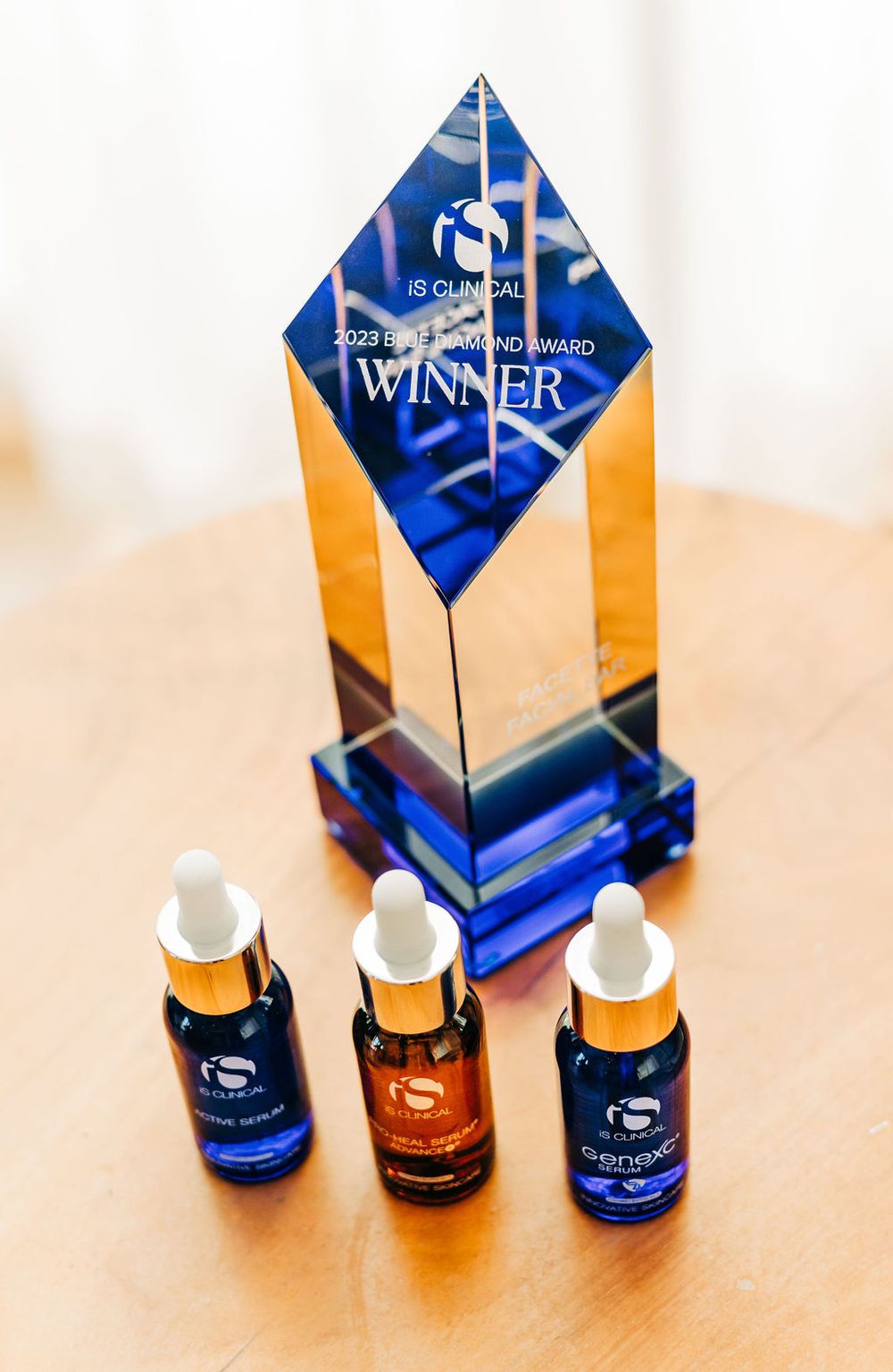 Blue and gold award trophy displayed with three dark glass dropper bottles of skincare serum.