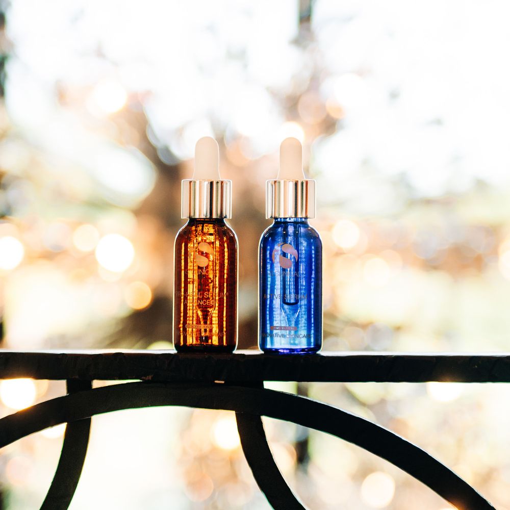 Two glass bottles in amber and blue colors sitting on a metal rail at sunset.