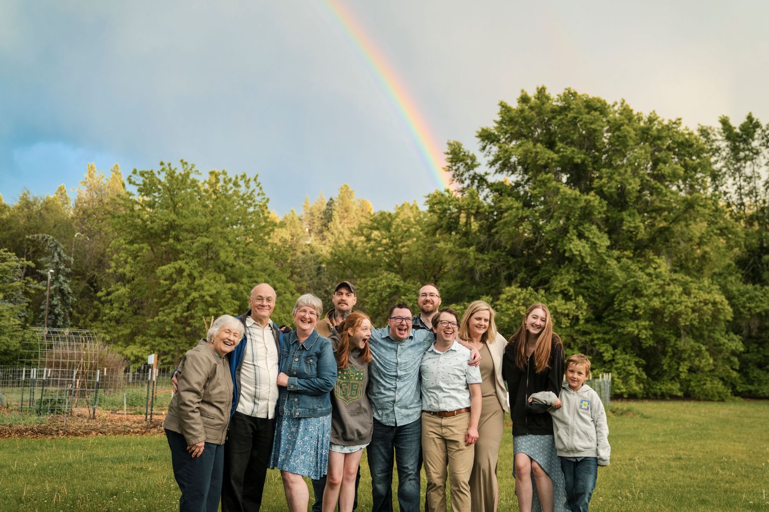 Group portrait with a beautiful rainbow arcing across the sky in a lush green field.