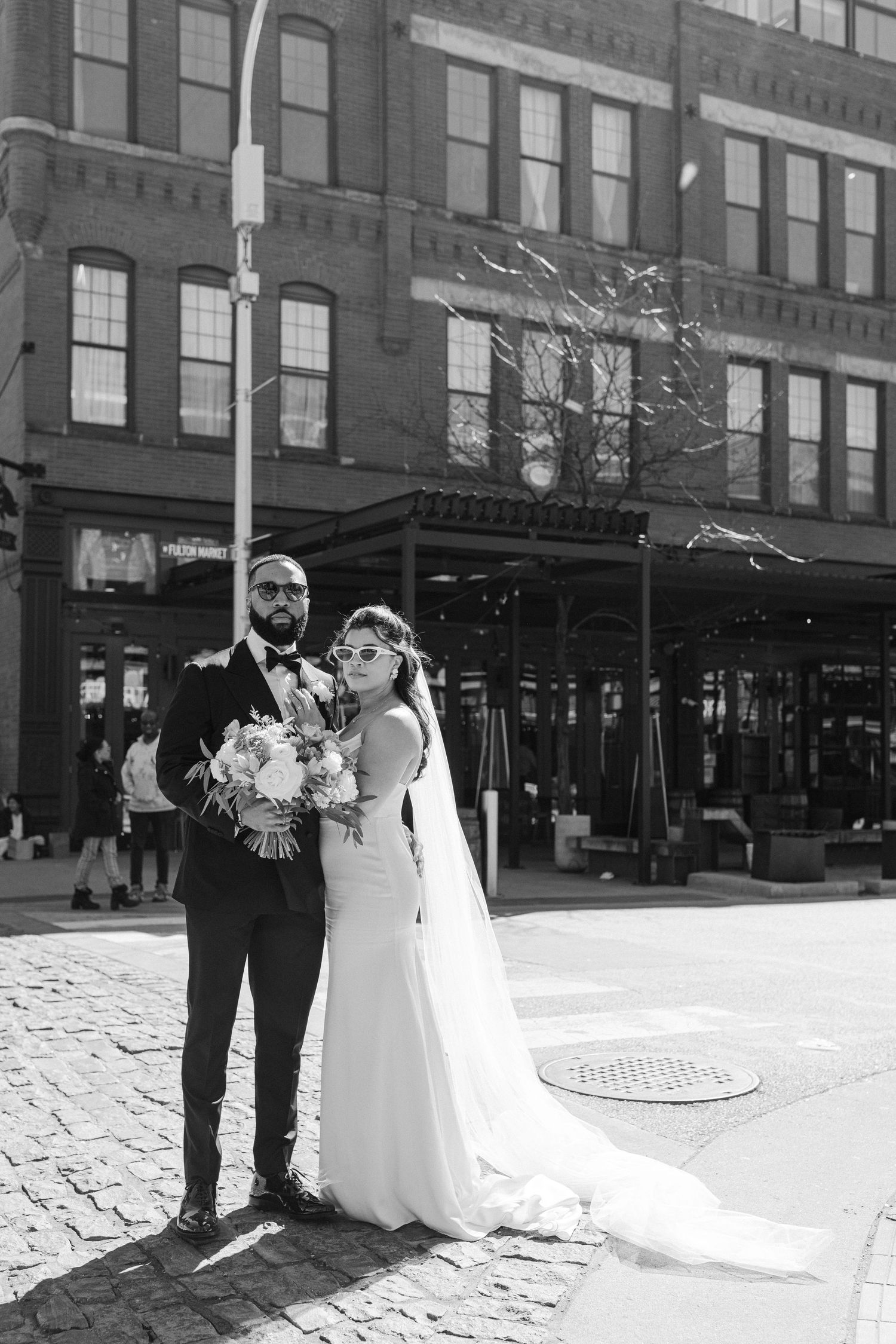 A wedding couple poses on a cobblestone street in front of historic brick buildings.