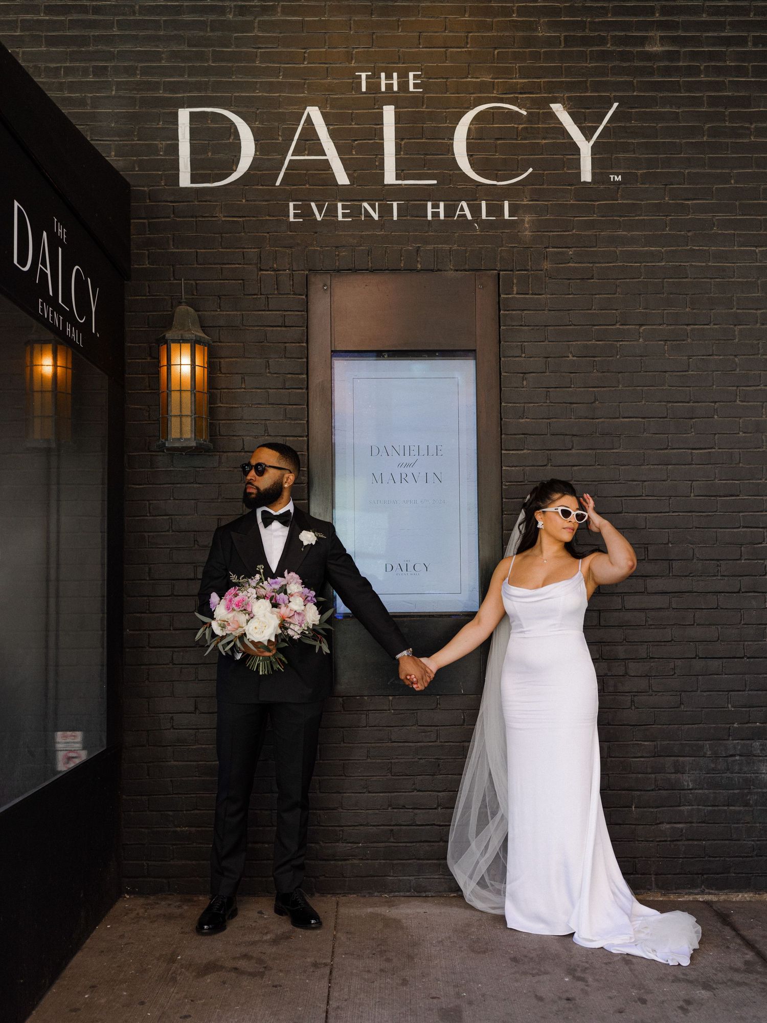 A couple takes stylish wedding photos outside The Dalcy event hall entrance.